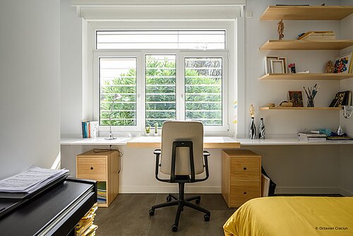The photo shows a small, cozy home office with plenty of natural light. At the desk is the AT swivel chair with gray upholstery.
