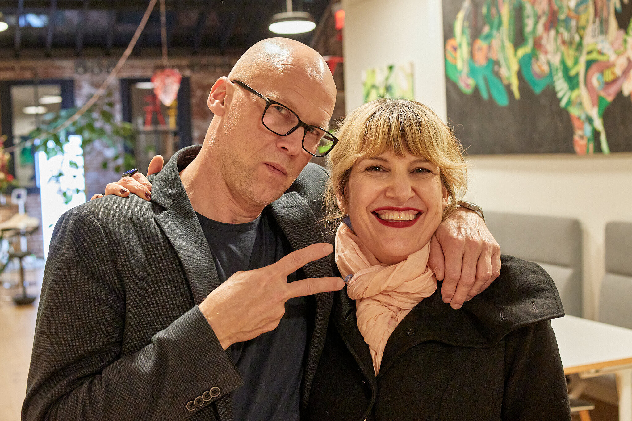 It is a picture of a man with his arm around a woman. The woman is smiling at the camera. The two of them are standing in an open hall.