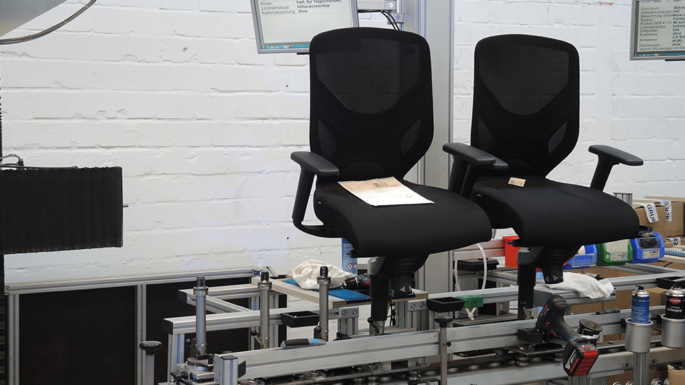This is a photo of two black IN swivel chairs that are currently being assembled in a fixture in our production facility.