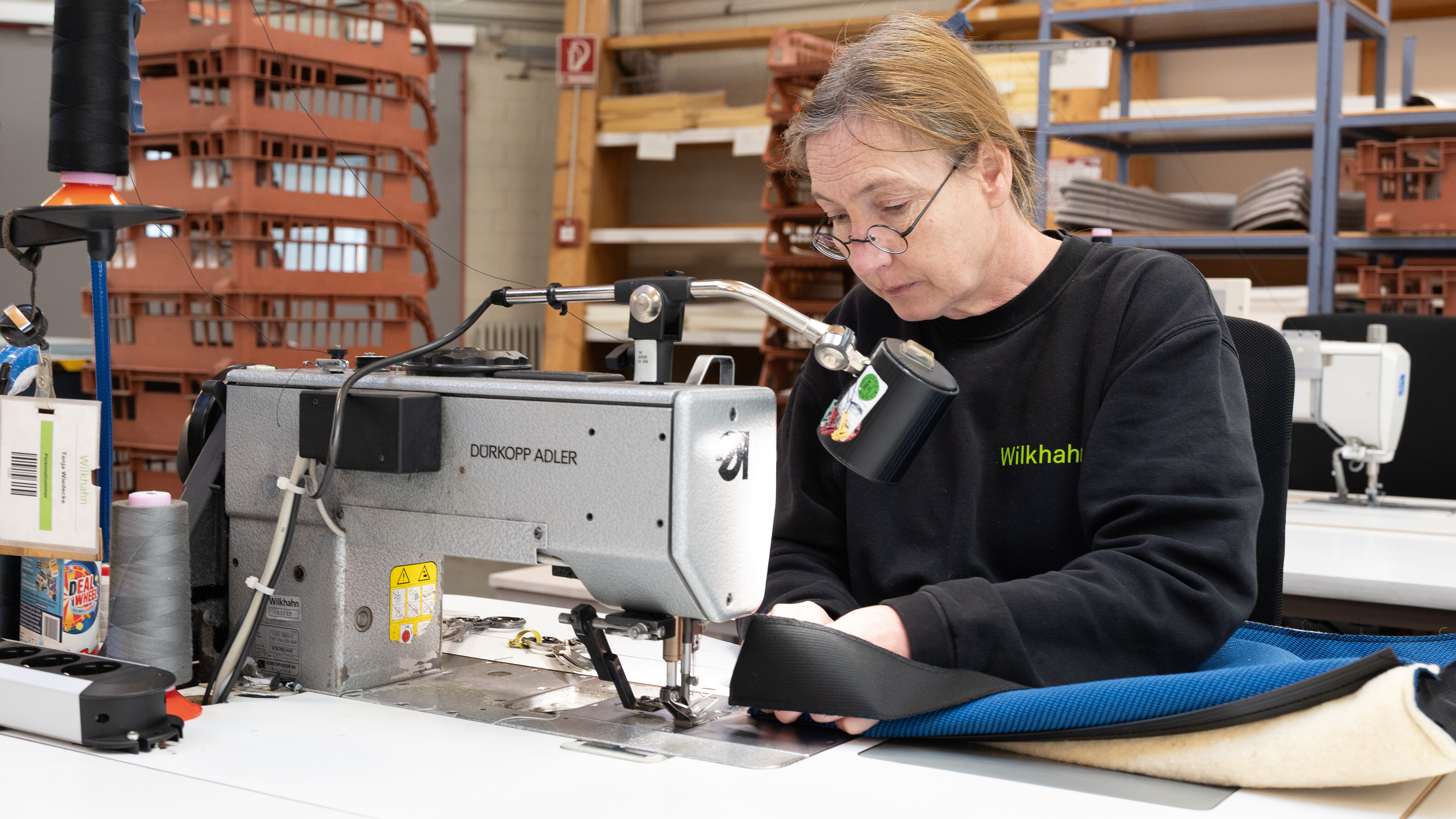 A close-up of a woman sewing the upholstery together. The upholstery is blue.