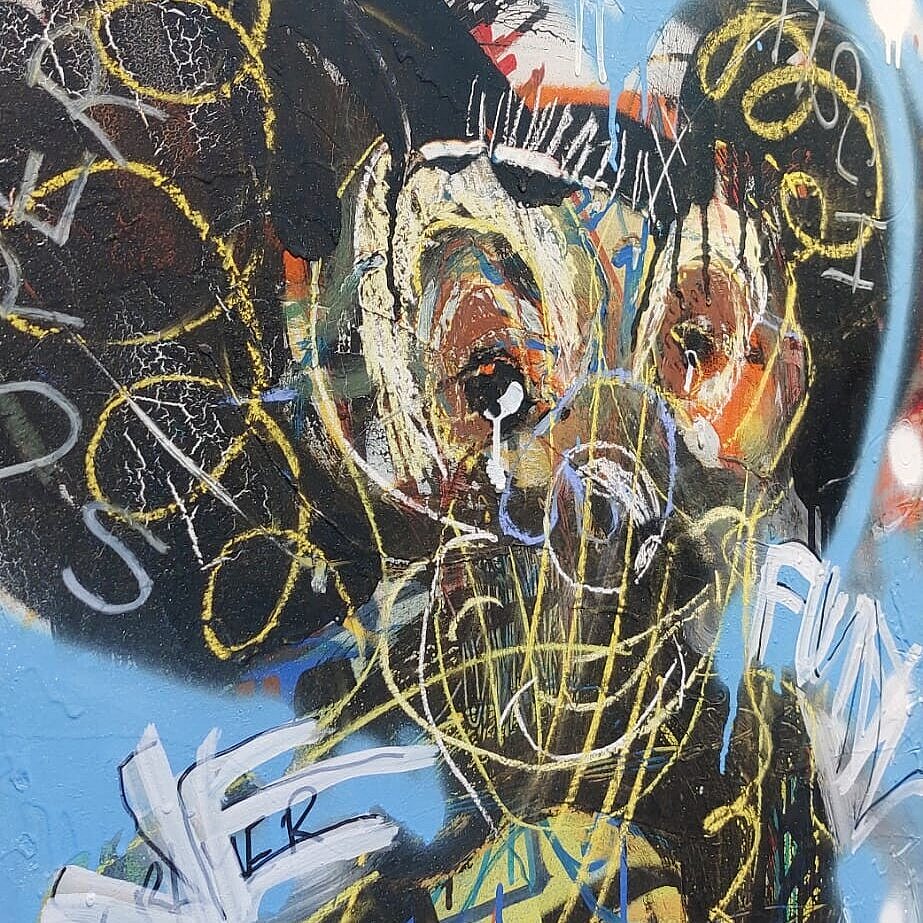 A close-up of a graffiti image depicting a human torso with large ears on its head. The image is predominantly black, blue, and yellow.