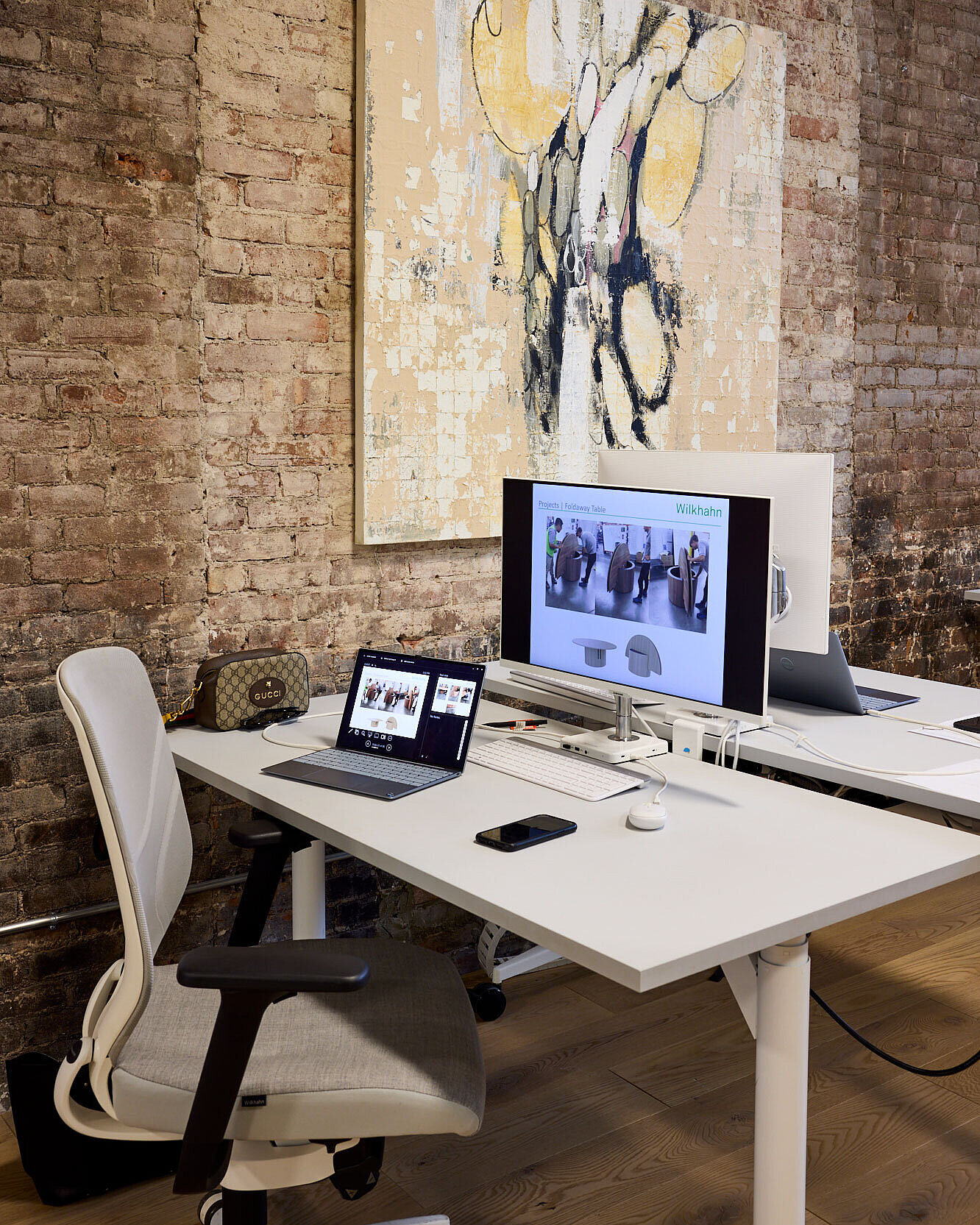 Two white tables stand in front of a brown brick wall. In front of one of the tables is a gray-and-white IN swivel chair.