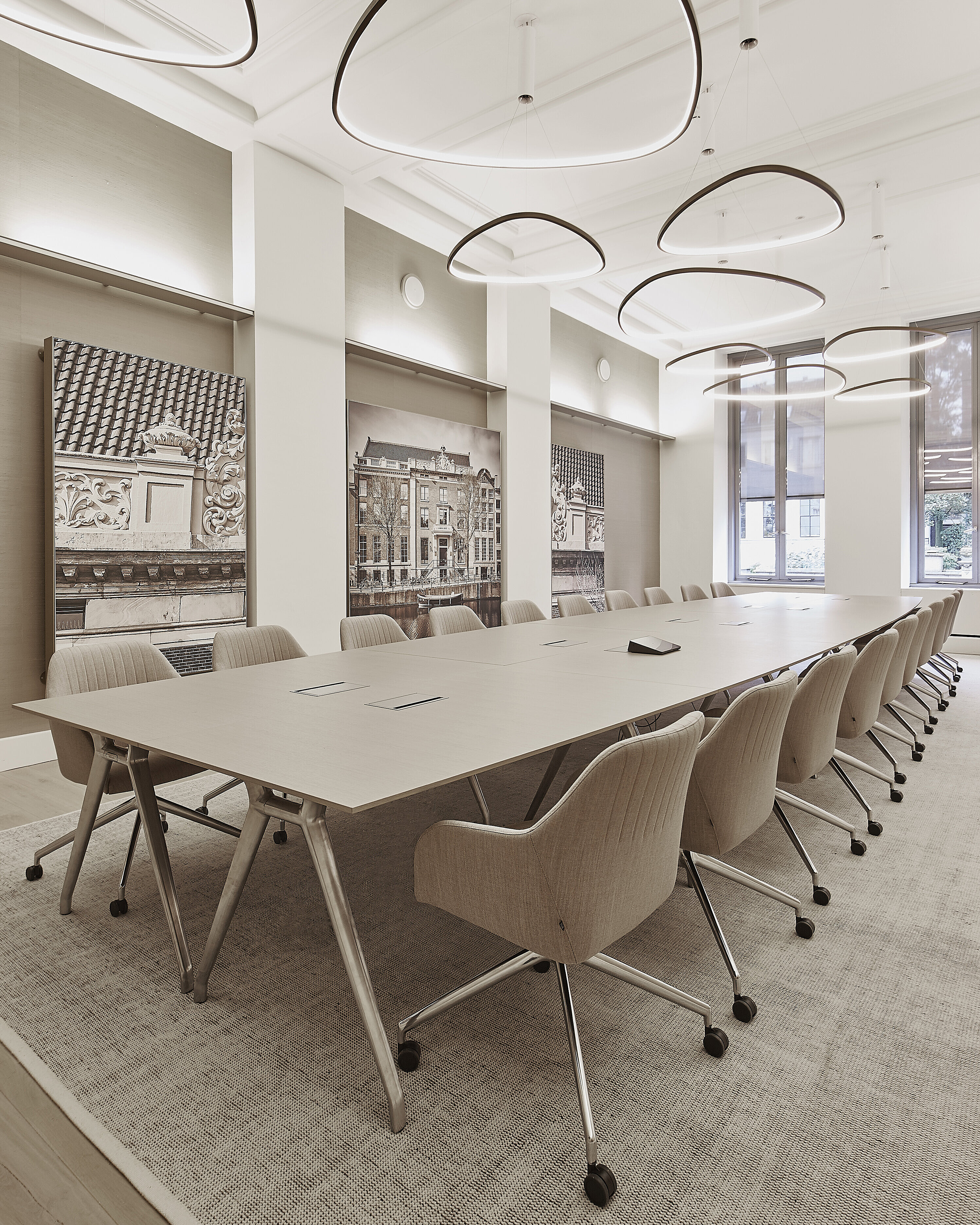 The photo shows a spacious, bright conference room with a long table and beige upholstered swivel chairs on casters. These are the Yonda conference chairs. The large, sculptural light fixtures and wall art give the room an elegant, modern touch.