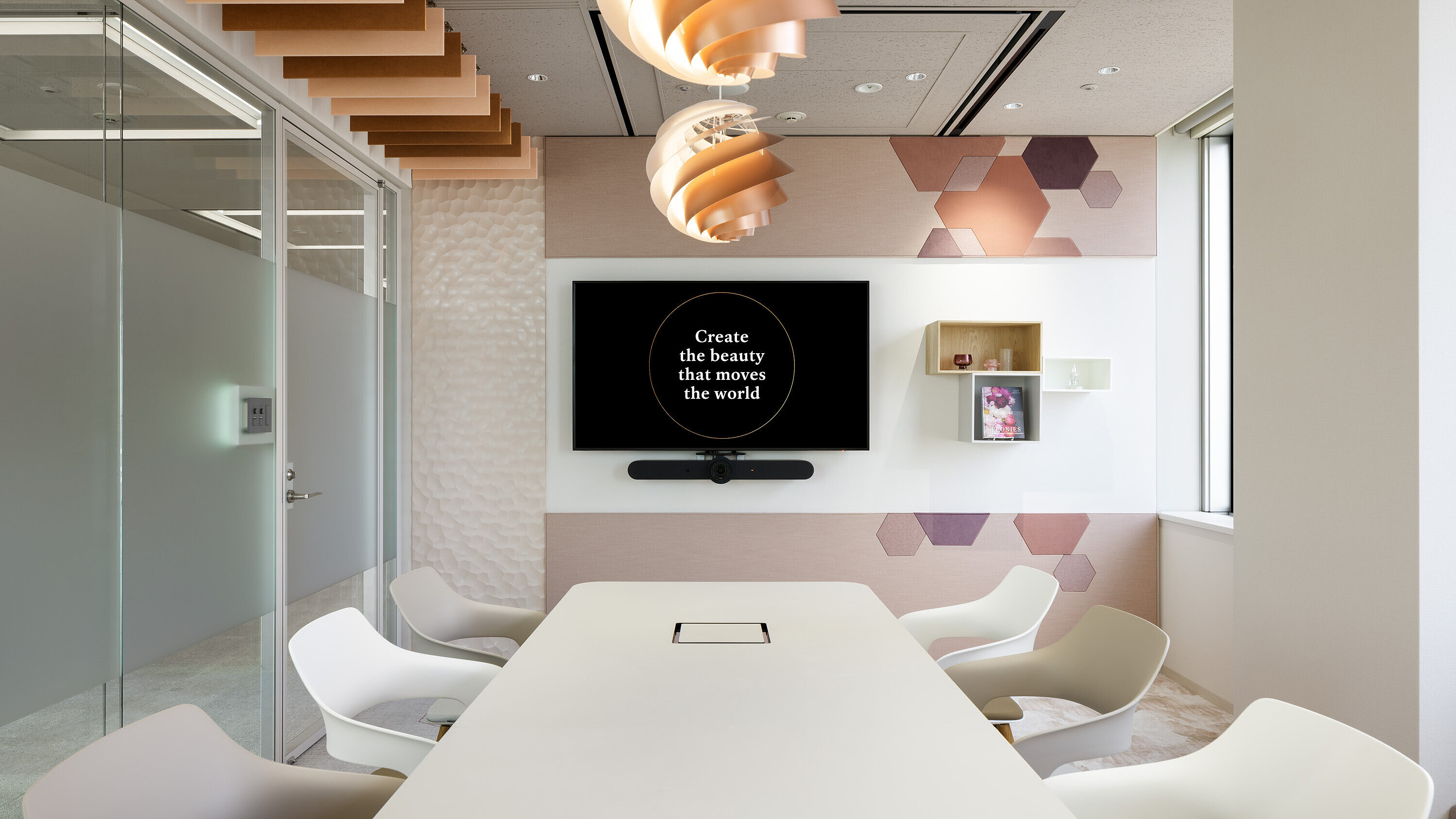 Occo chairs with beige or white seat shells are arranged around a long white conference table. In the background, a monitor hangs on a pastel pink wall.