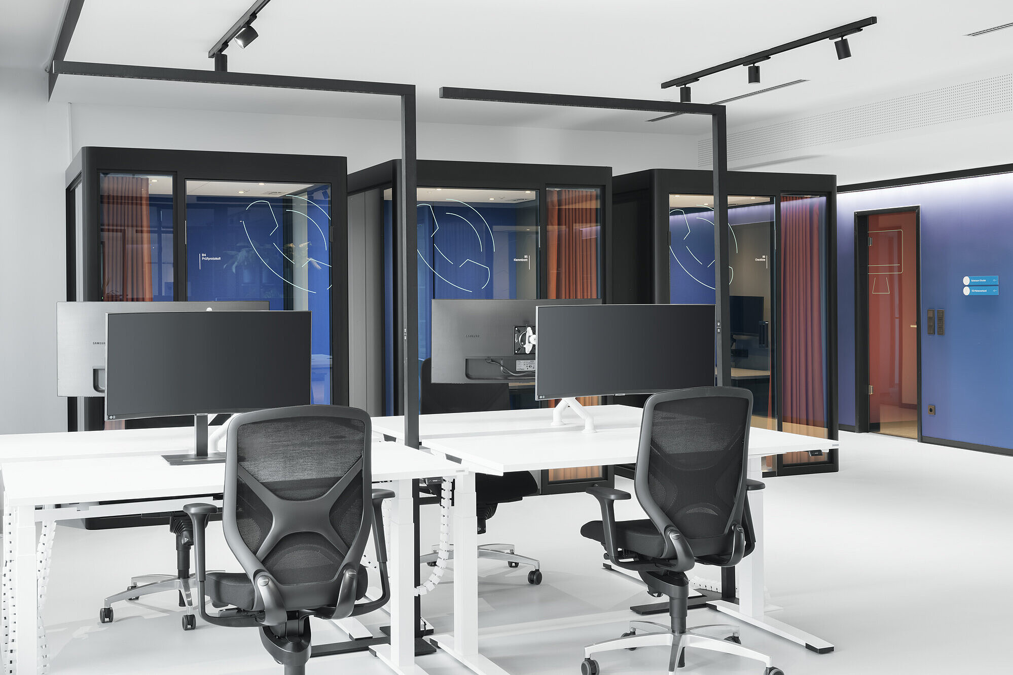The modern open-plan workspace is furnished with IN swivel chairs, recognizable by their distinctive backrest design and synchronous movement mechanism. The clean lines and glass meeting pods create a futuristic, very uncluttered work environment. The chairs add functional, ergonomic accents to the space.