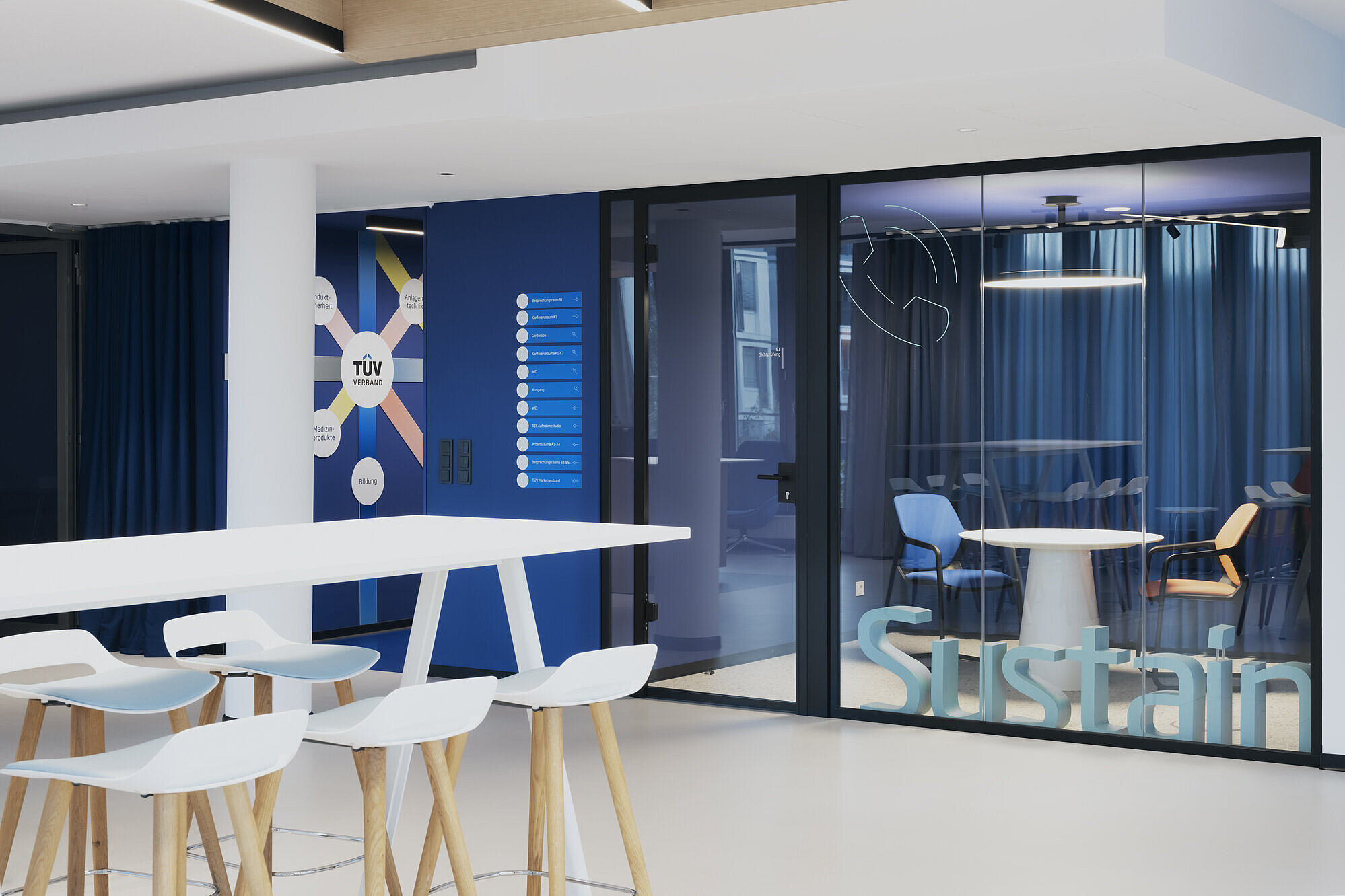 The entrance or reception area combines light-colored materials with colorful accents. Occo bar stools are visible in the foreground. Behind the glass wall in the background are Metrik cantilever chairs, which add a splash of color to the open meeting area.