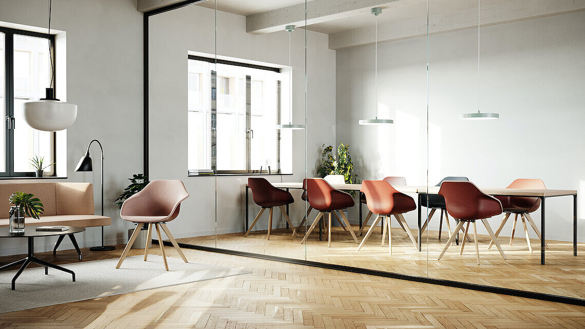 The meeting room is open, flooded with natural light, and features warm wooden accents. Surrounding the table are several Yonda chairs with wooden frames and red seat shells.