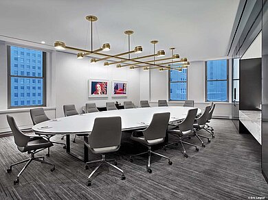 A conference room with a round white table and many light gray Graph chairs with low backrests.