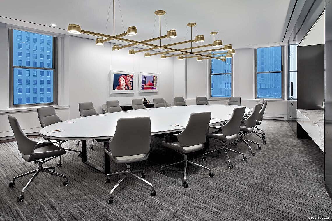 A conference room with a round white table and many light gray Graph chairs with low backrests.