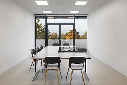 The bright meeting room features a clean, minimalist design with large windows and plenty of natural light. The black Occo chairs, with wooden legs and light-colored upholstery, are commonly used in conference rooms. The room has a modern, calm, and functional feel.