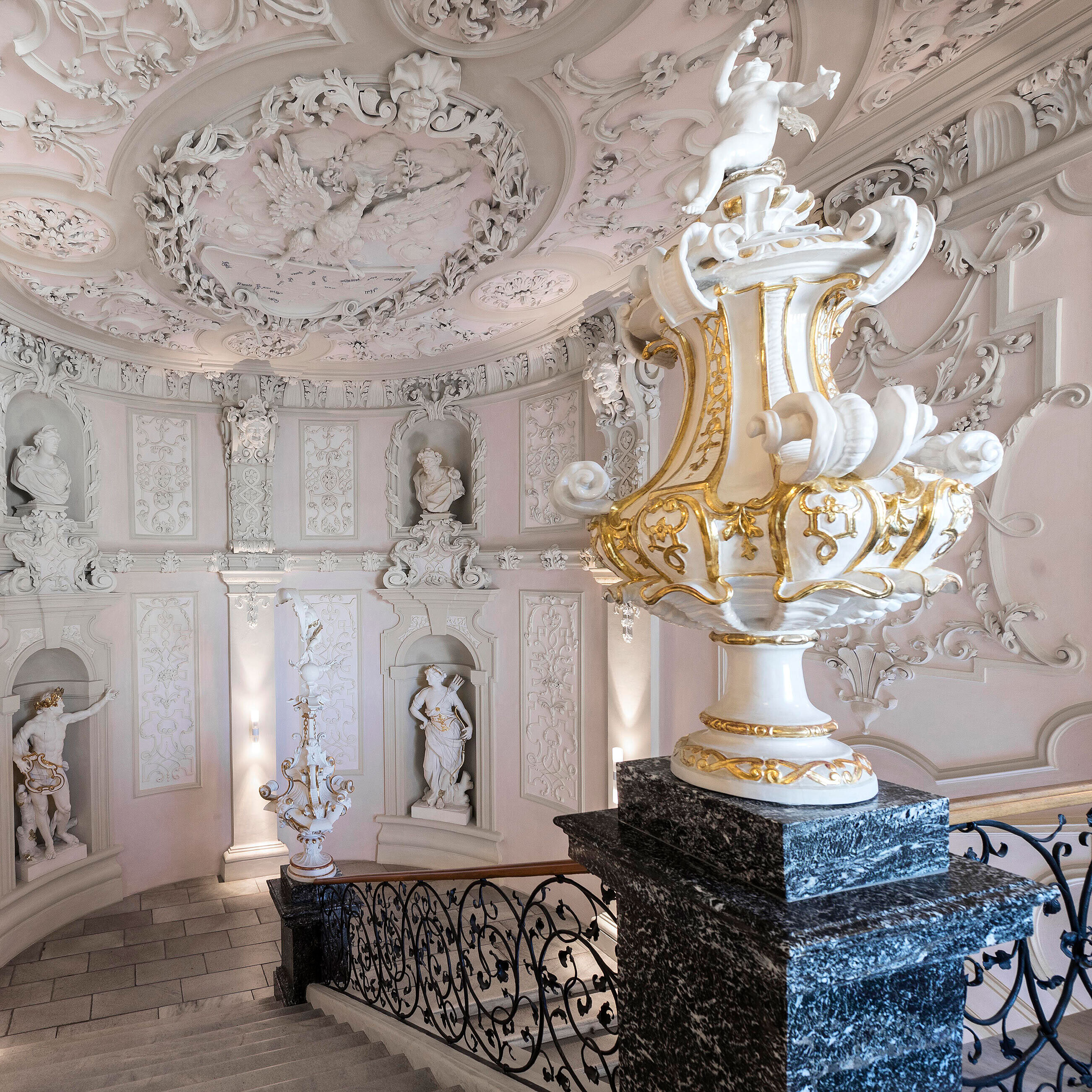 A stairwell with white walls featuring elaborate wall decorations, as well as statues of angels and gods.