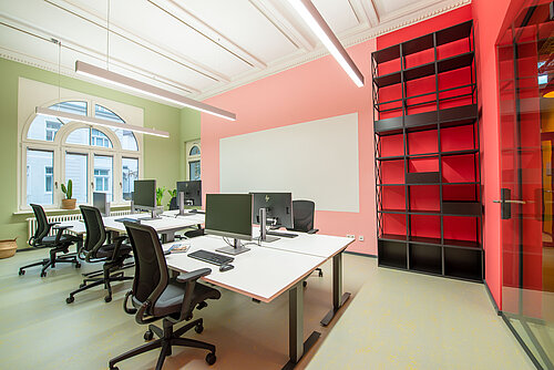 The walls in the office are green and red. In the middle are several tables with black IN swivel chairs.