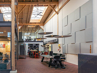 A view of the interior of an office building. On the right is a break area featuring a black table with three black FS chairs. On the left and in the background are office spaces furnished with black AT chairs. The interior design style is industrial.