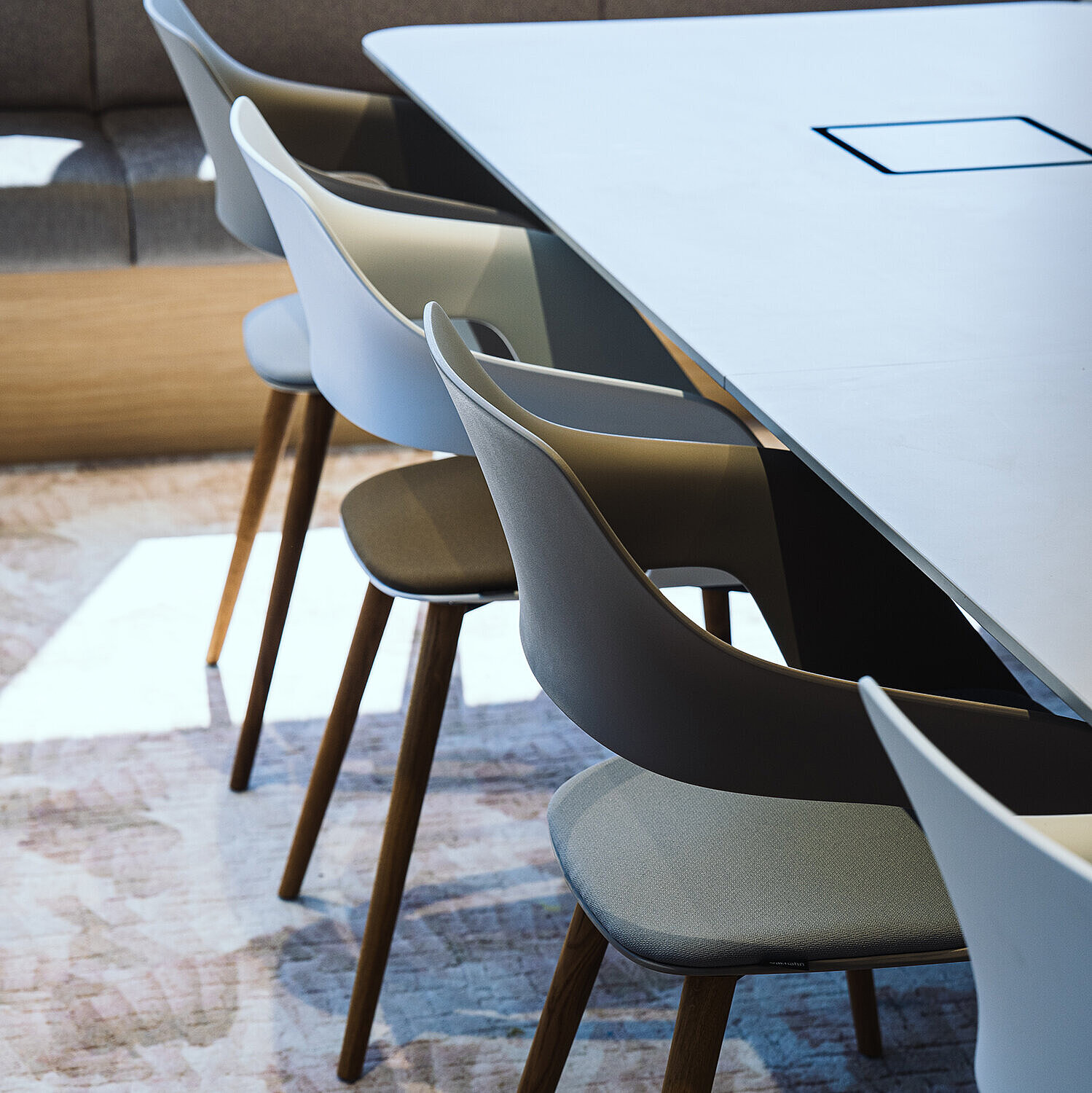 Occo chairs with white or gray seat shells and seat pads in shades of green are arranged around a white table. Die Stühle haben ein Vierfußgestell aus Holz.