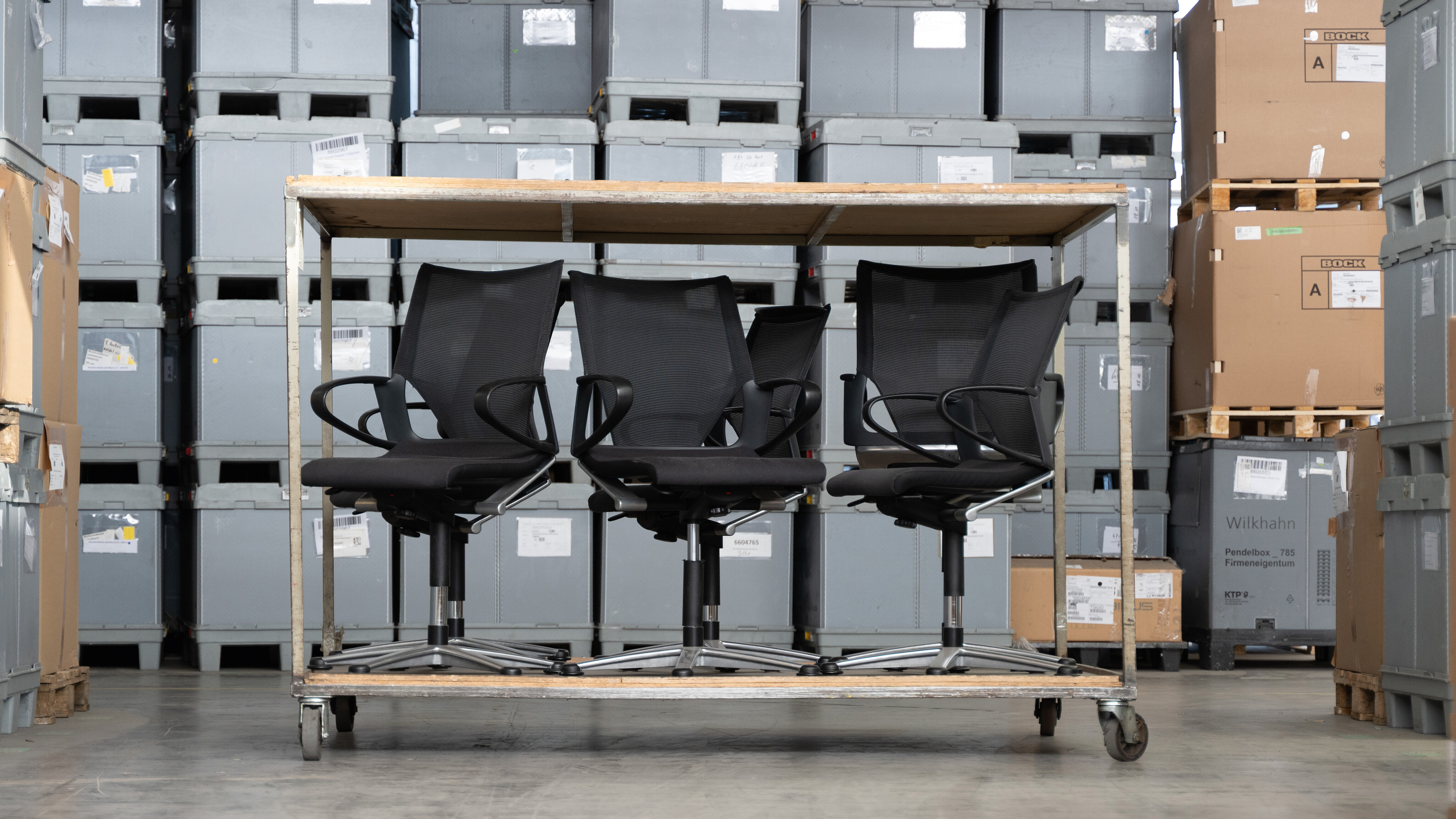 Several black swivel chairs are on the lower level of a double-decker carriage. In the background, gray boxes can be seen in a warehouse.