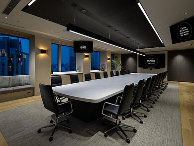 In a large conference room, several Sola conference chairs upholstered in black leather are arranged around a long table with a white tabletop.