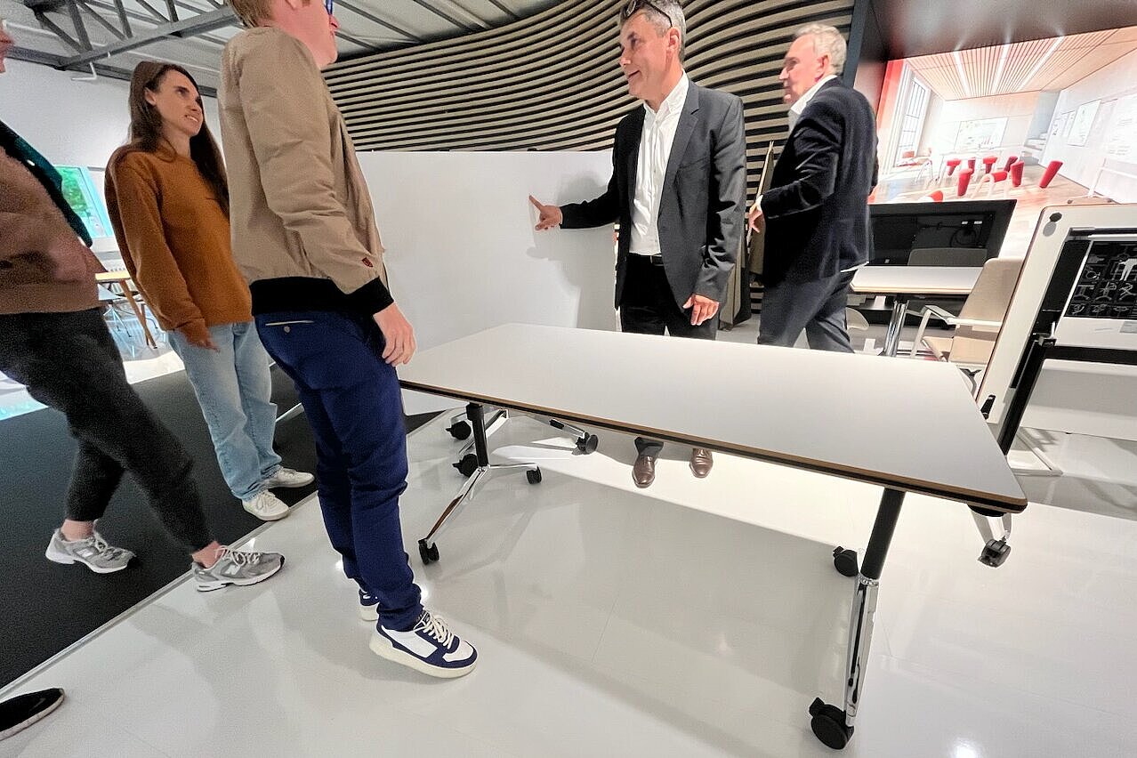 A group is looking at a Timetable folding table that is currently being presented by Lutz Präger. The focus is on the intuitive folding mechanism and the high-quality craftsmanship. The setting suggests that this is a demonstration in the showroom in Eimbeckhausen.