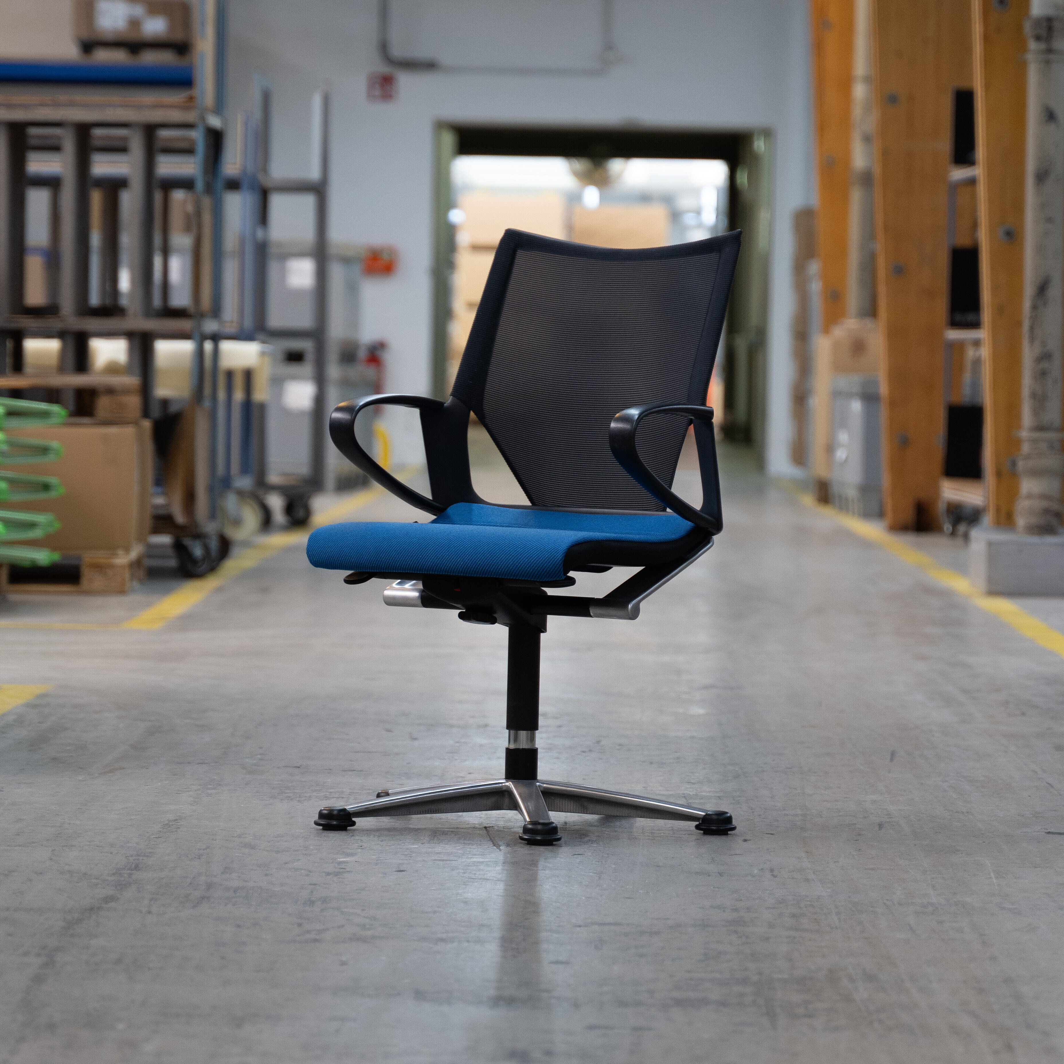 A Modus chair stands alone in the assembly hall. The back is black and the seat upholstery is blue.