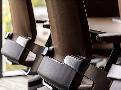 A close-up of two ON swivel chairs with brown leatherand a close-up photo of an brown armrest.