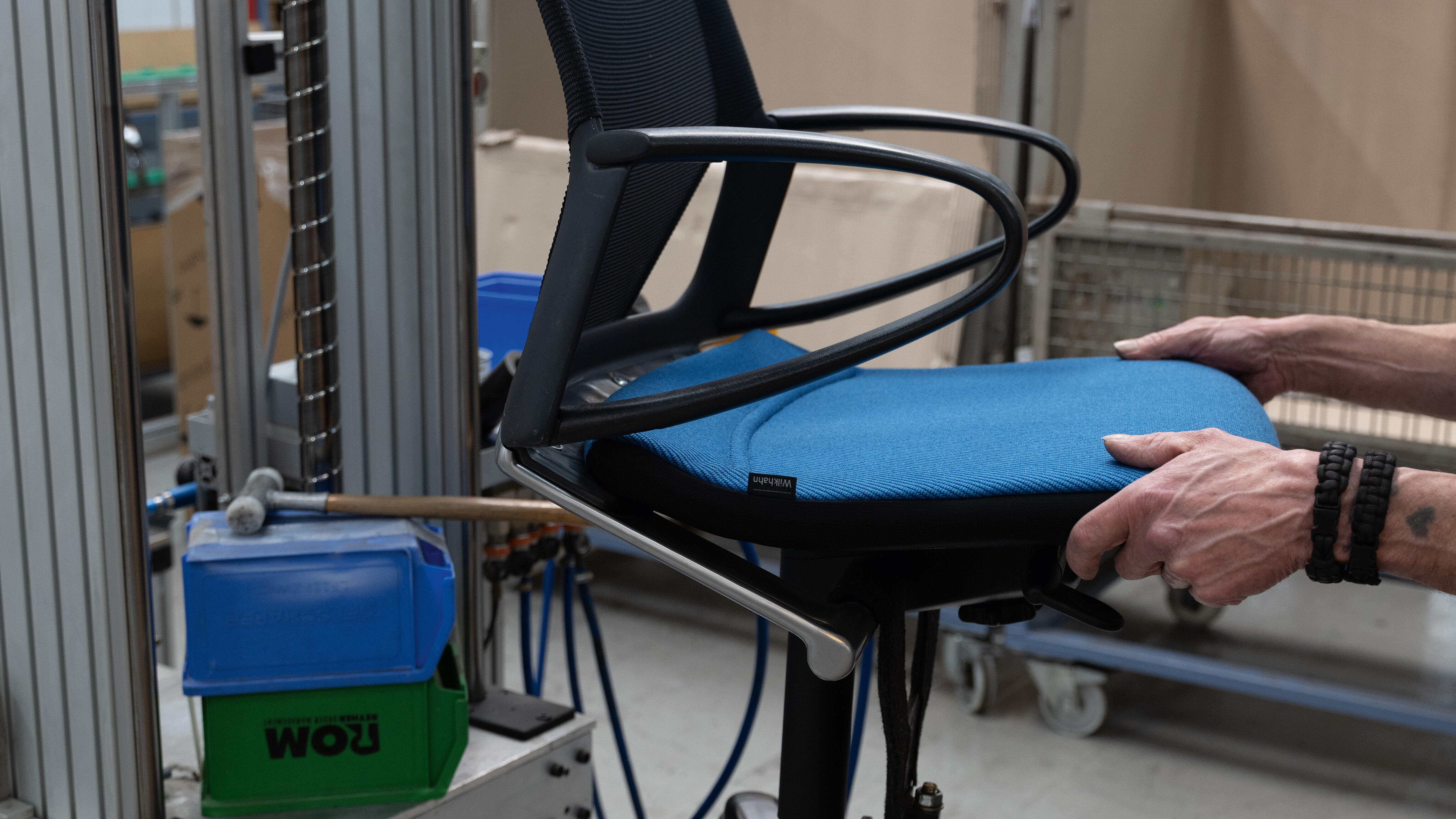 A close-up of the Modus chair being installed. The chair has a black frame and a blue seat pad.