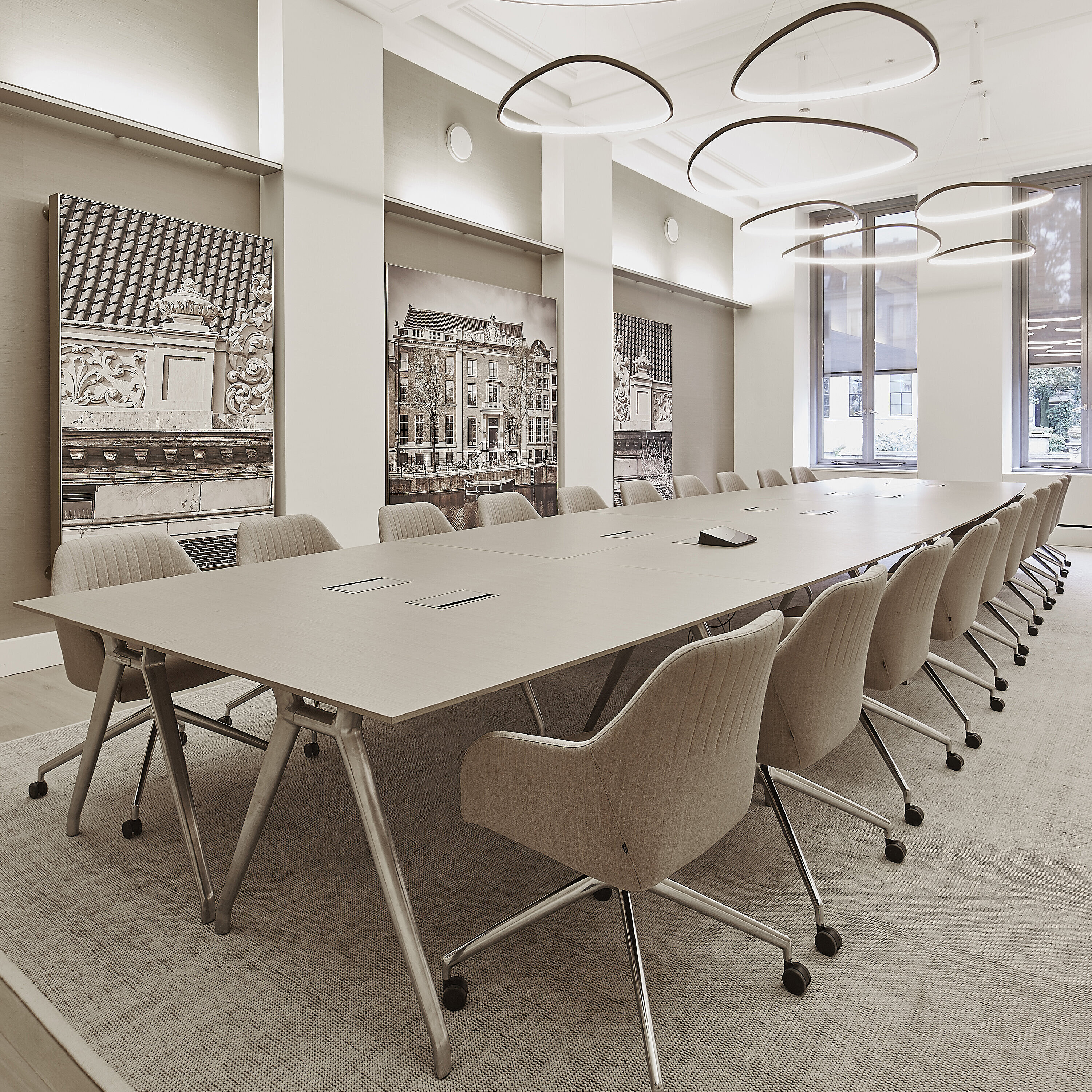 The photo shows a spacious, bright conference room with a long table and beige upholstered swivel chairs on casters. These are the Yonda conference chairs. The large, sculptural light fixtures and wall art give the room an elegant, modern touch.