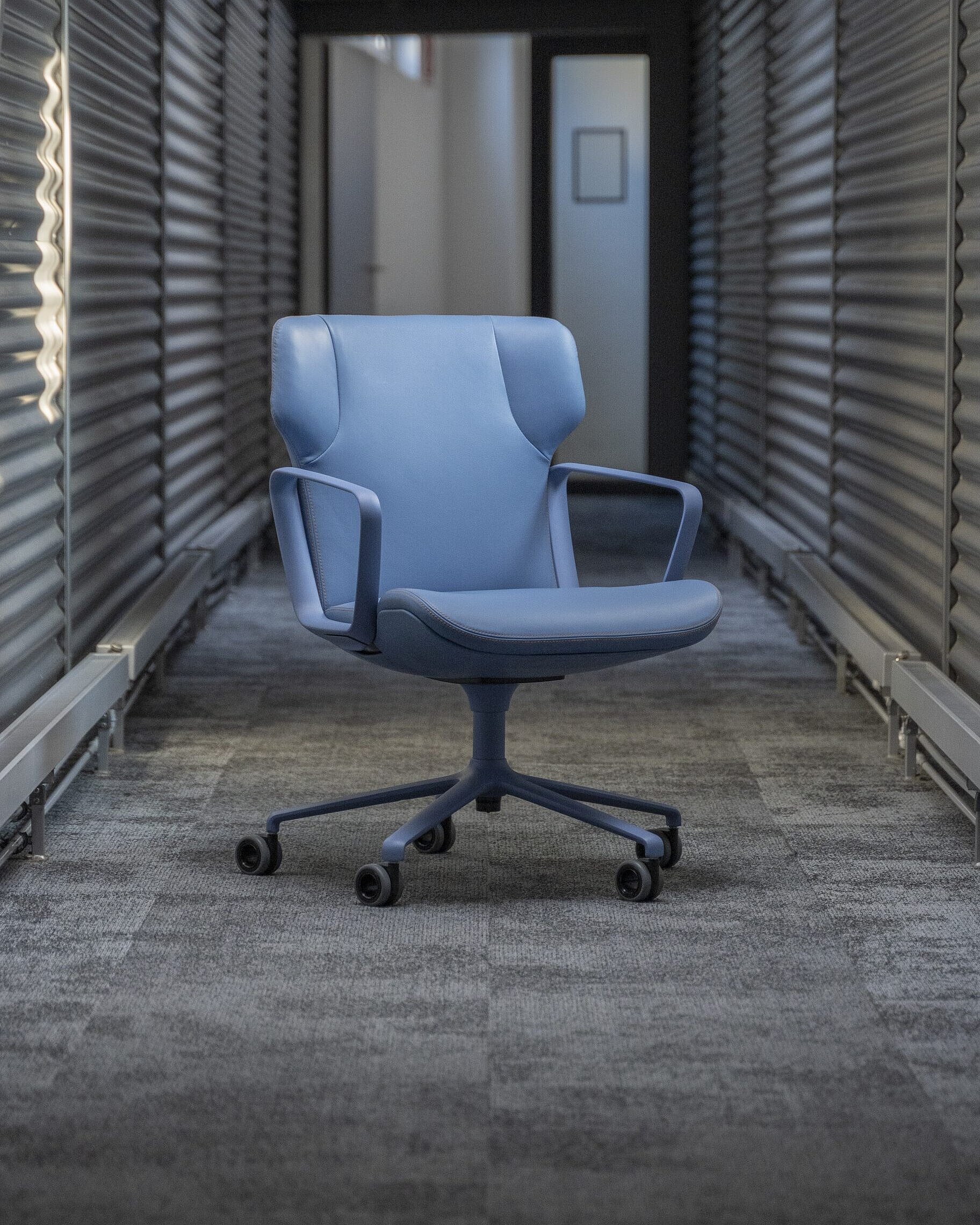 An Intra armchair upholstered in blue leather stands in a hallway with gray floors and walls.