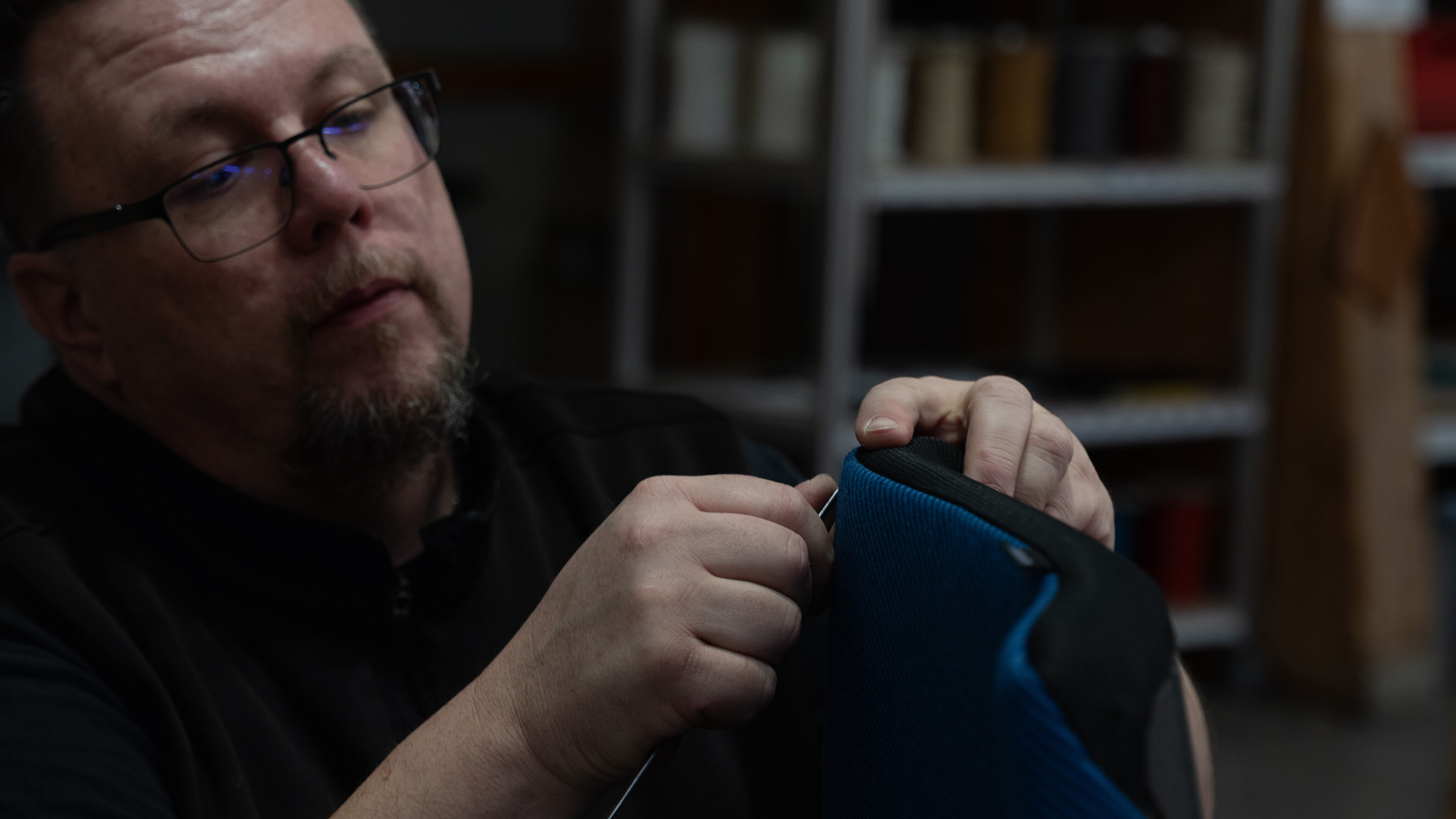 A close-up of someone upholstering a chair. The upholstery is black and blue.