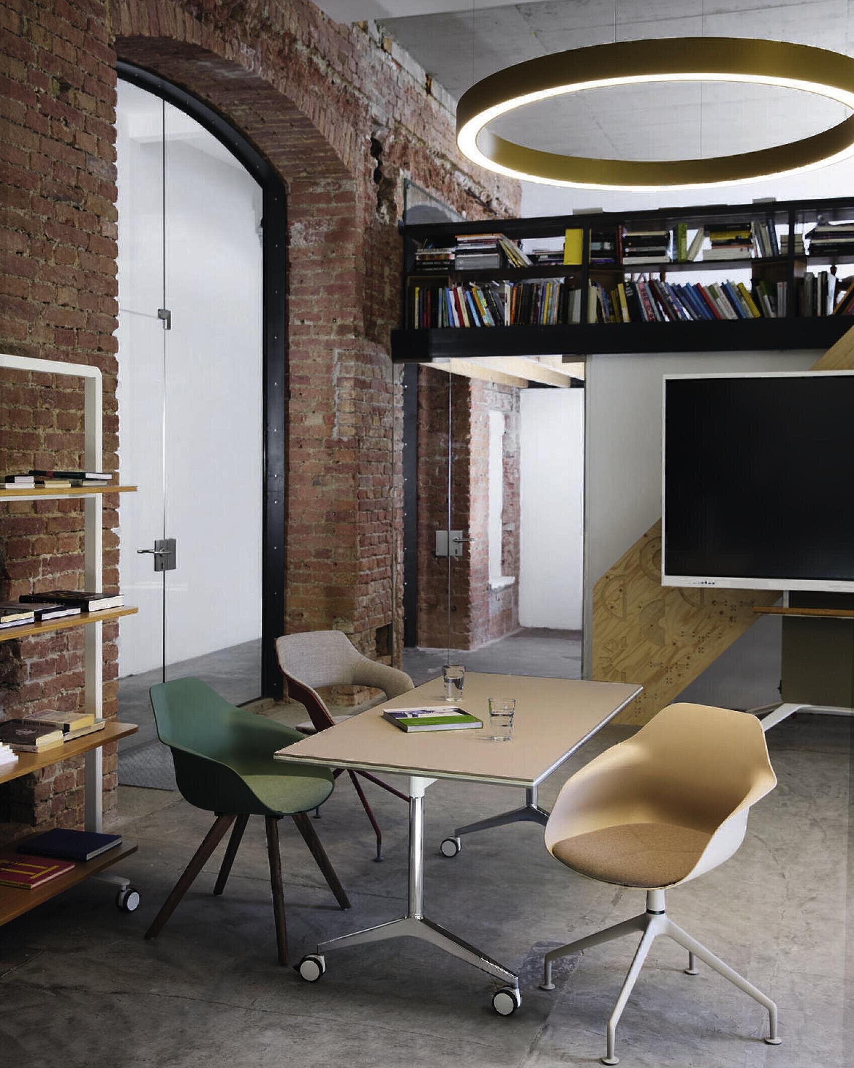 In an office, there is a Timetable table with two Yonda chairs—one with a beige seat shell and one with a green seat shell—and an Occo chair with beige seat and back upholstery. The room has an industrial design.