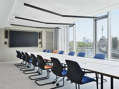 The large conference room is furnished with a row of Metrik cantilever chairs, shown here in blue and orange. The large window wall in the background provides plenty of natural light and a view.