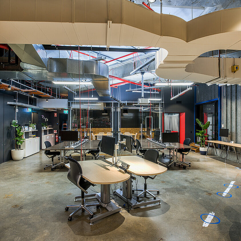 The photo shows a modern, open-concept office with several workstations and an industrial interior design. In the center are several desks, each equipped with black FS swivel chairs. The exposed wiring and ventilation ducts on the ceiling are visible.