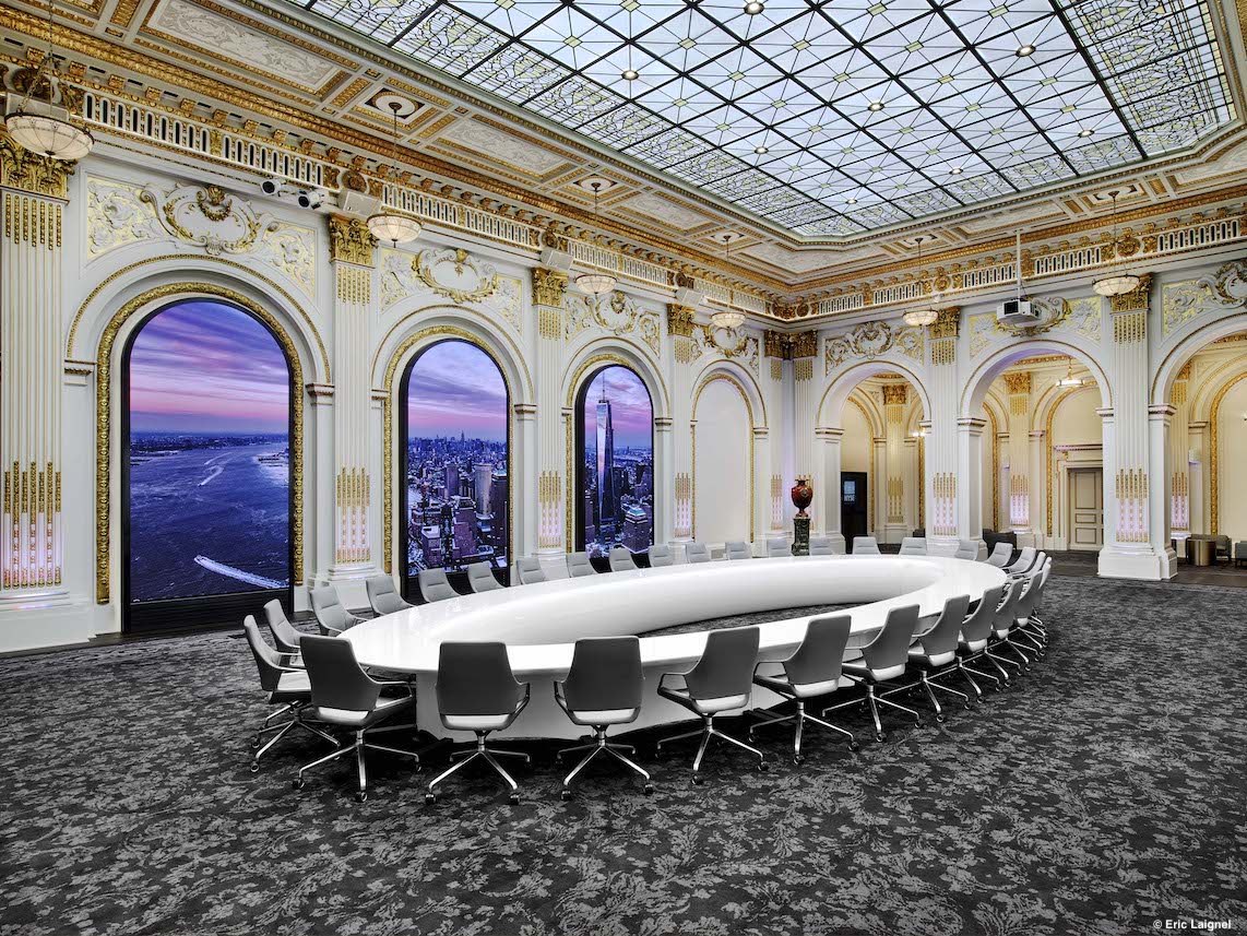 A large hall with a round white table and many light gray Graph chairs with low backrests.