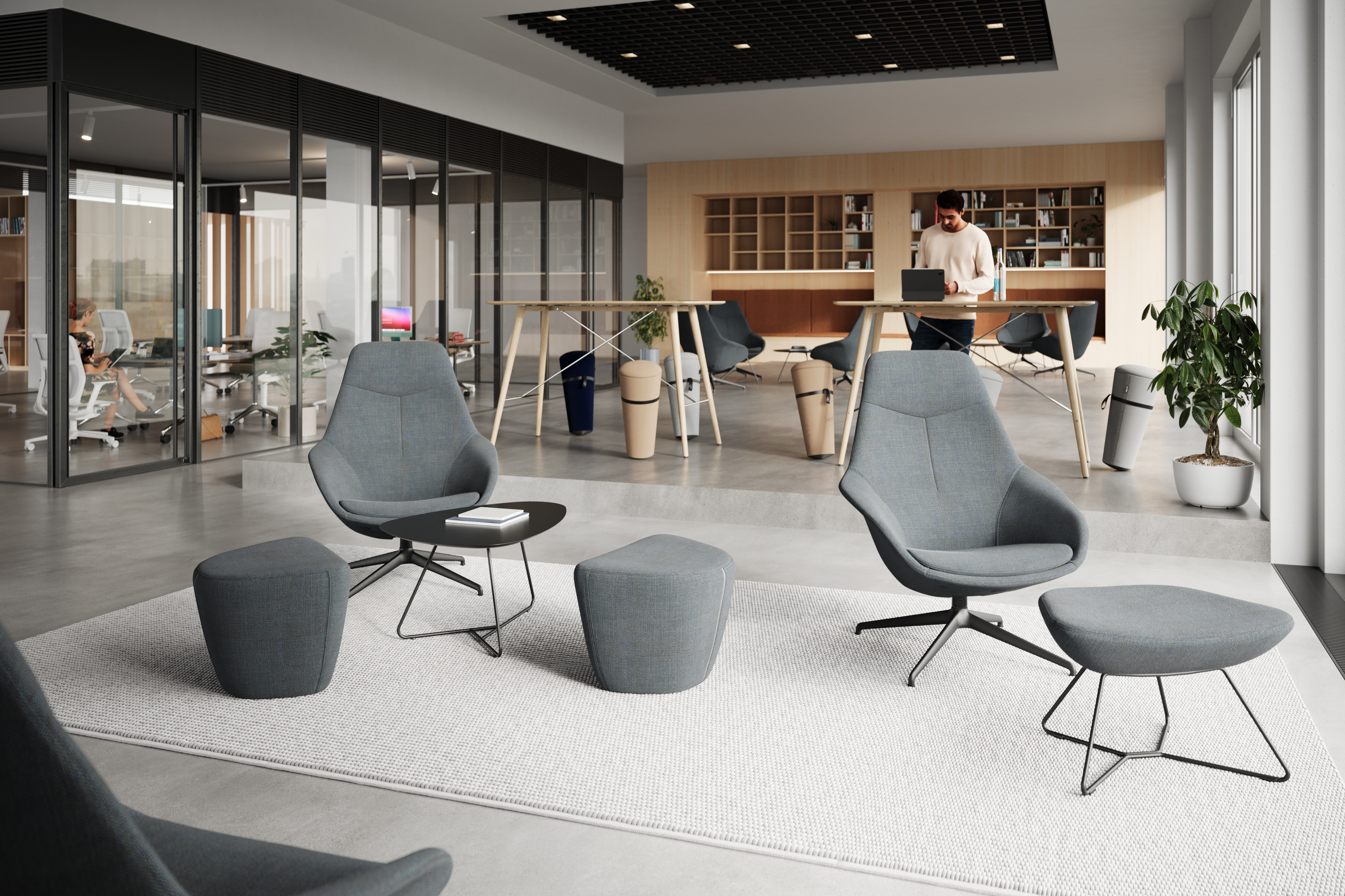 This is an open area in an office building. In the background, you can see gray, fully upholstered Yonda lounge chairs and Occo tables. In the foreground, the Yonda lounge chairs are visible in greater detail. In the adjacent office, white AT mesh chairs are visible.