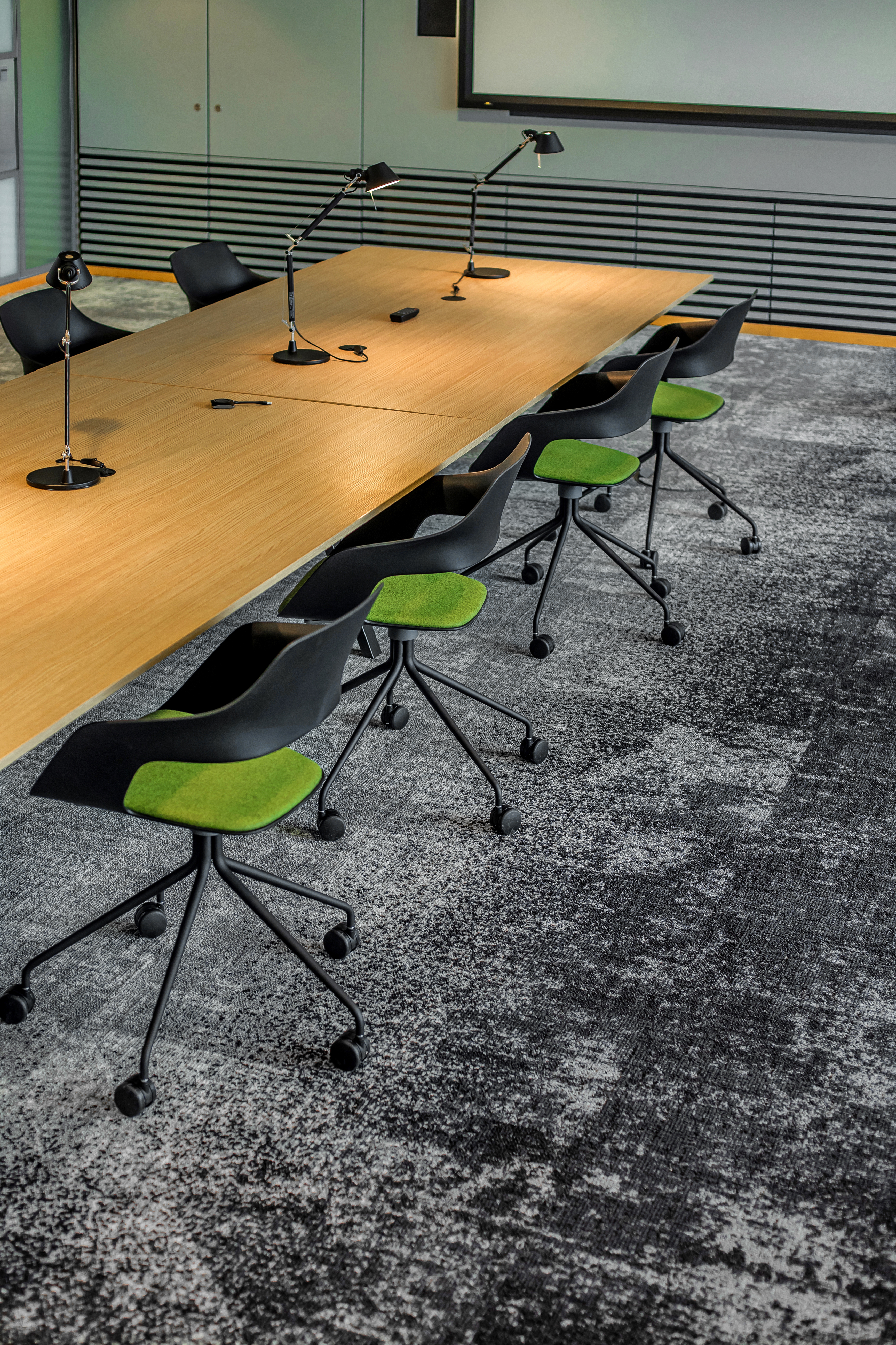 A table setup in a conference room with lamps on top and black Occo chairs arranged around it. The seat pads are green.