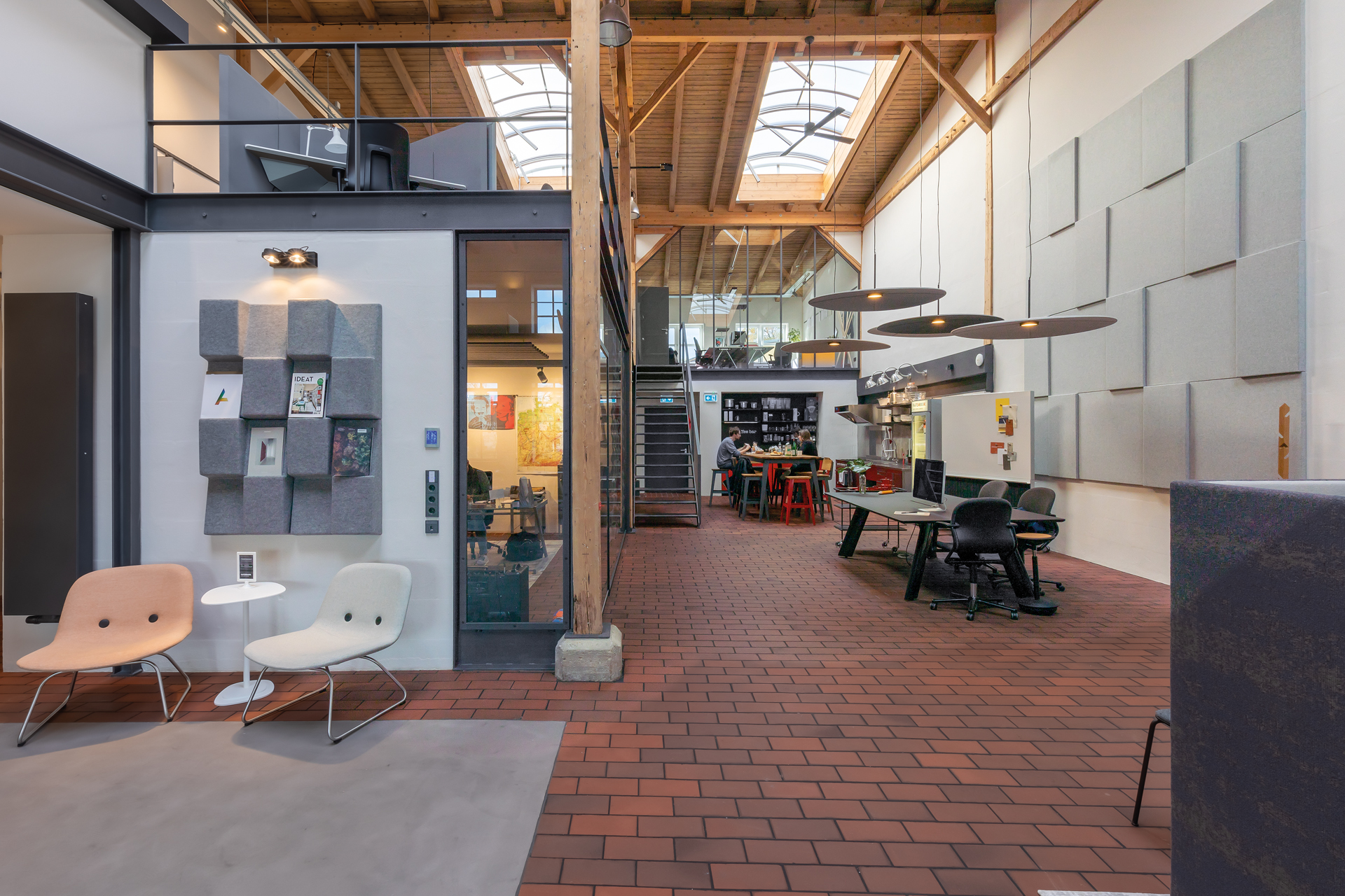 A view of the interior of an office building. On the right is a break area featuring a black table with three black FS chairs. On the left and in the background are office spaces furnished with black AT chairs. The interior design style is industrial.