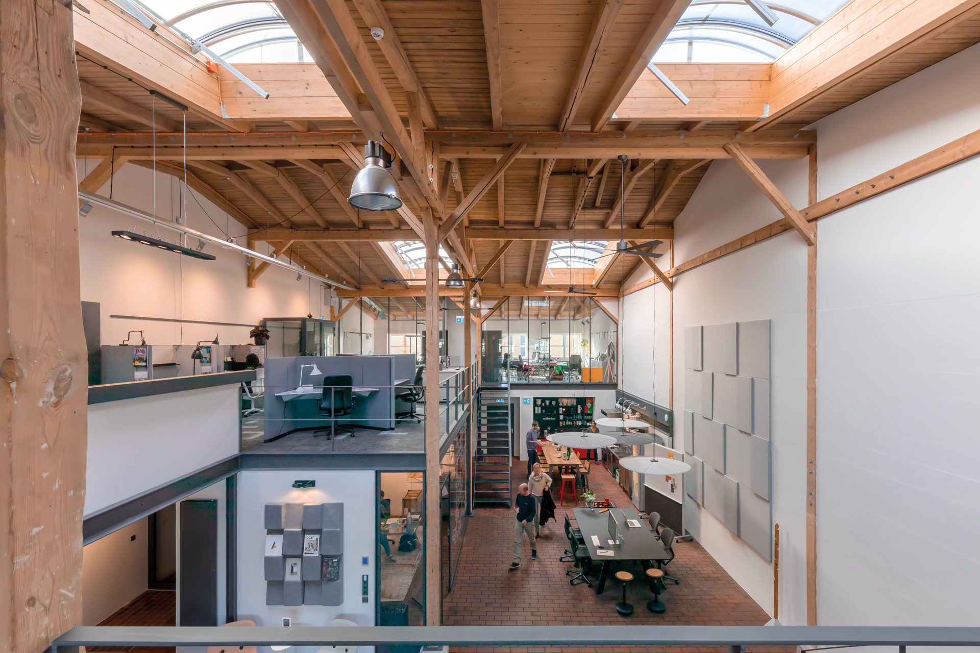 A view of the interior of an office building, photographed from above. On the right is a break area featuring a black table with three black FS chairs. On the left and in the background are office spaces furnished with black AT chairs. The interior design style is industrial.