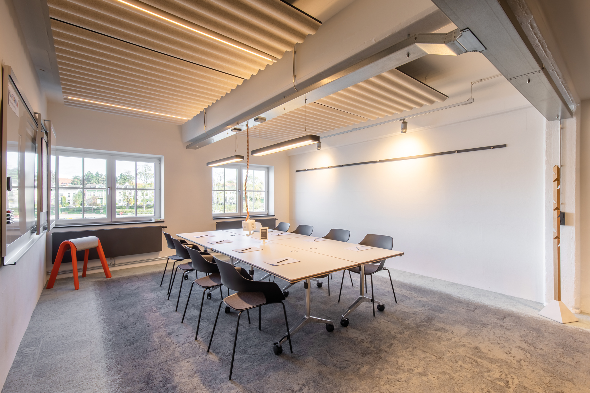 A view of a conference room with four white Timetable tables and eight black Occo chairs without upholstery. There is a red Sitzbock in the corner on the left.