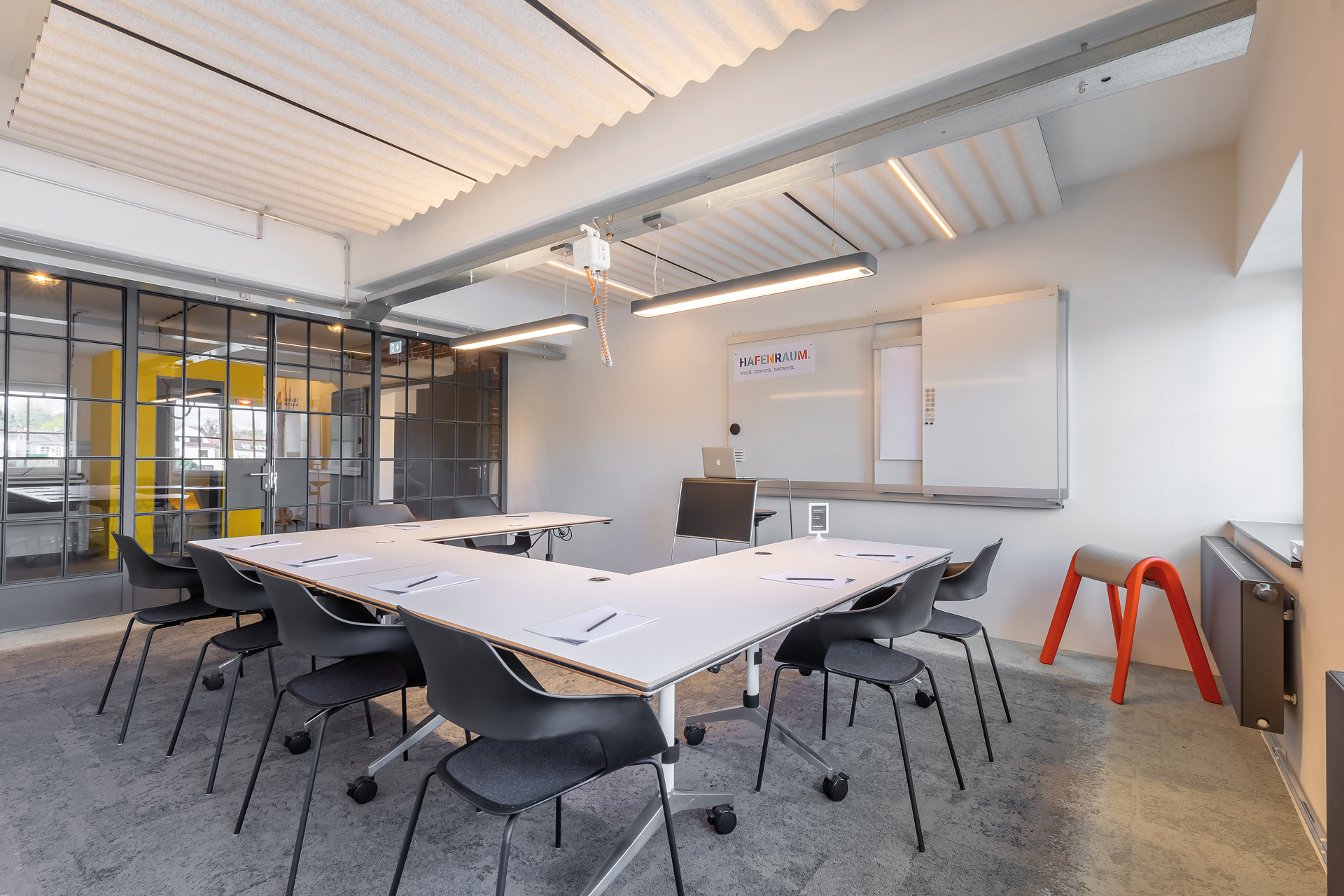 In this conference room, four white Timetable tables are arranged in a U-shape, with eight black Occos placed around them. A speaker's podium stands at the front.