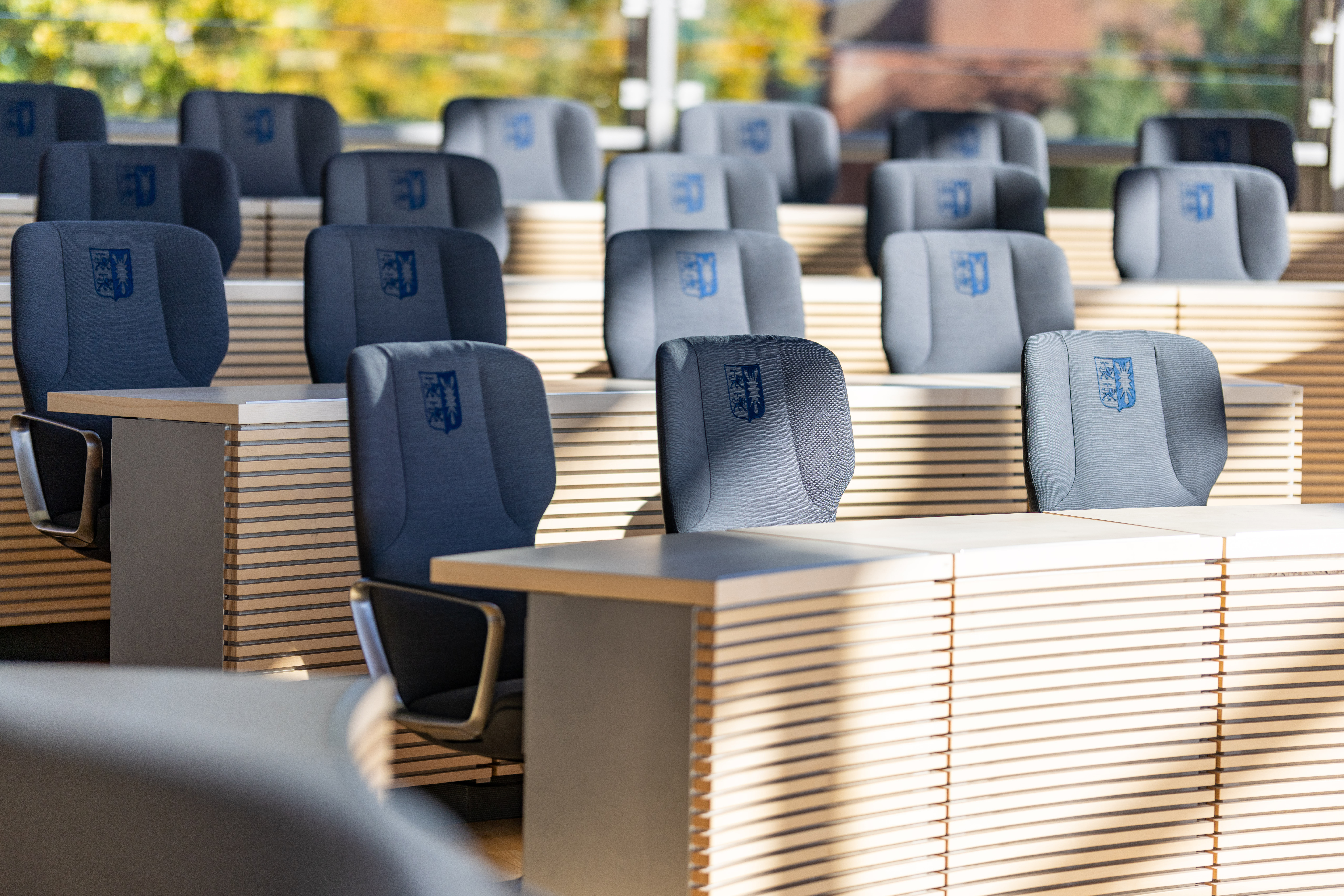 A close-up of the Intra conference chairs arranged behind the wooden tables. Each chair has an embroidered coat of arms of the Kiel State Parliament.