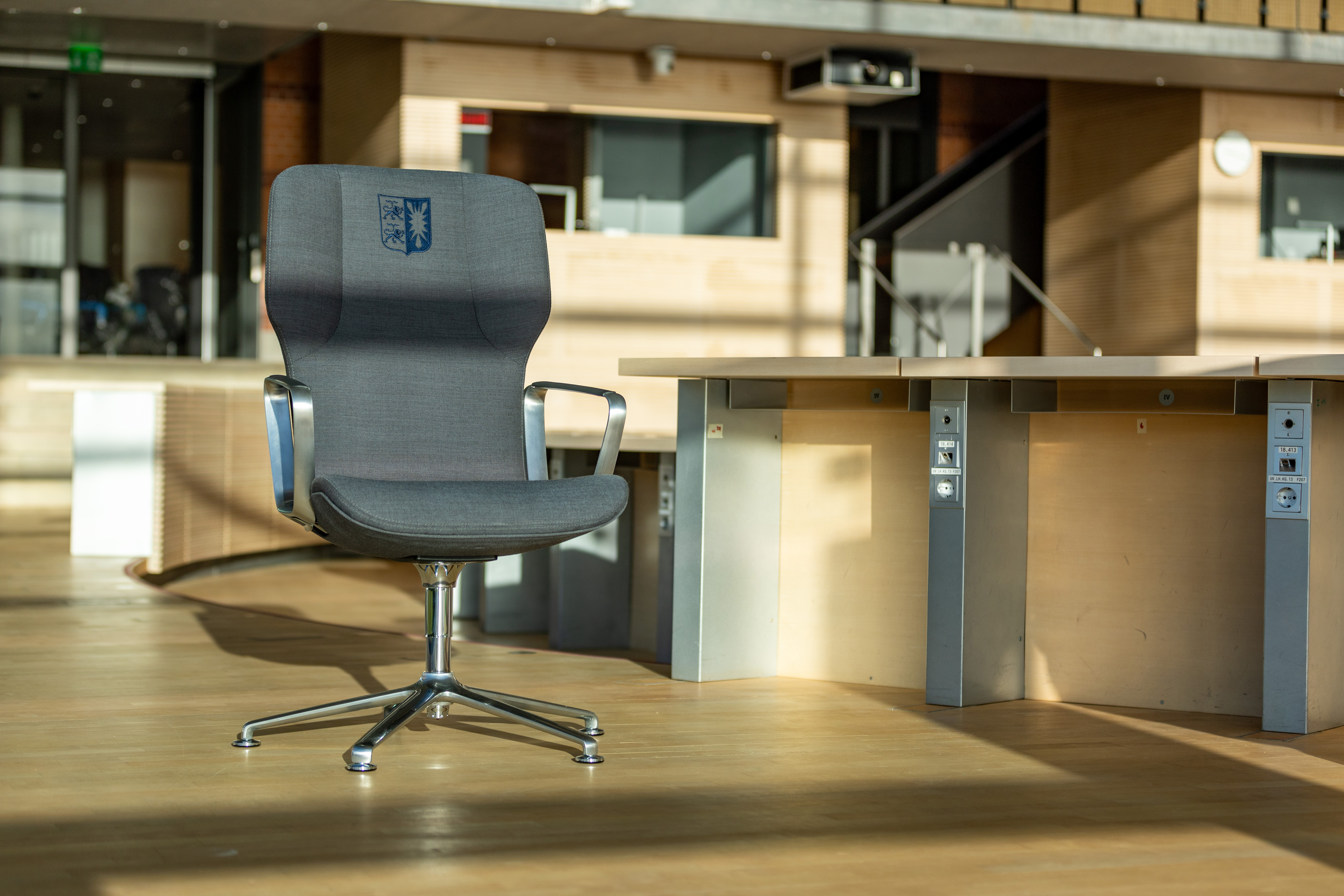 A gray Intra conference chair with the Kiel State Parliament’s coat of arms embroidered on it stands in the State Parliament chamber.