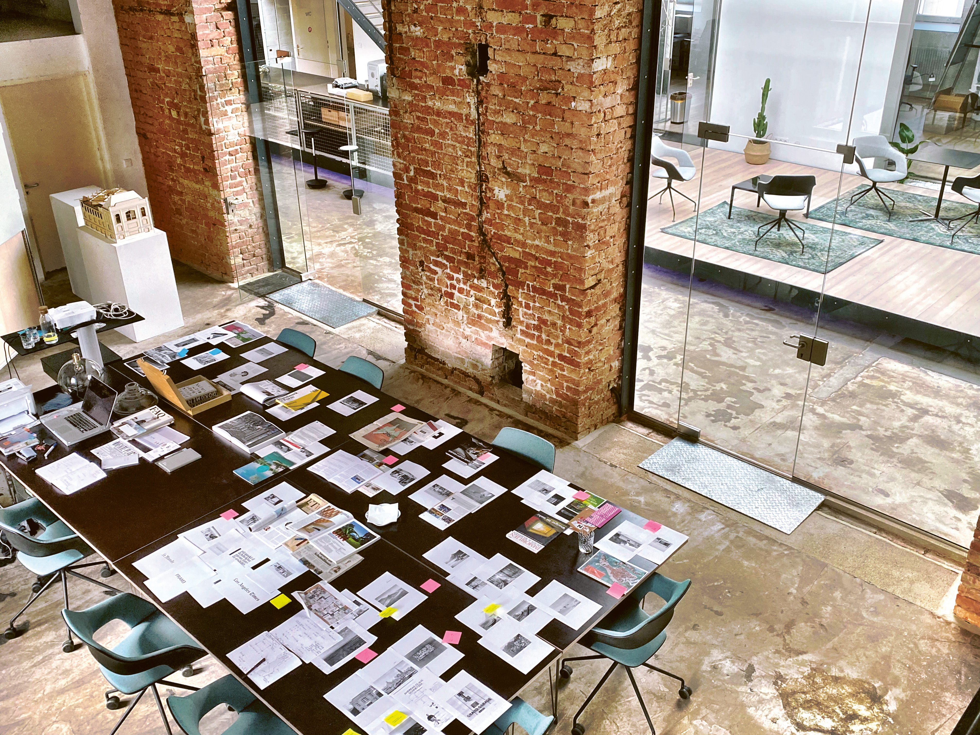 The view is from above, showing a long black table in an industrially styled meeting room, with several sheets of paper bearing notes and Post-its scattered across it. Surrounding the table are Occo chairs with black seat shells and light blue seat and back upholstery.