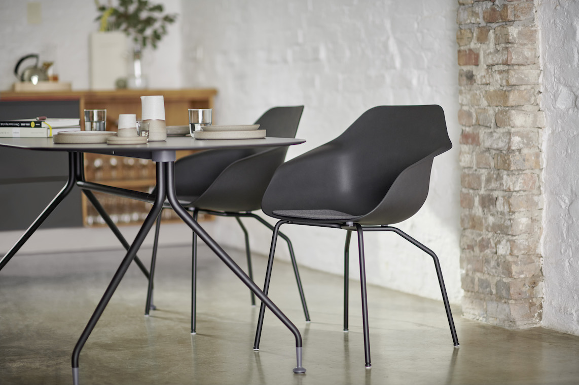The modern room features two black Yonda chairs with four-legged steel frames. The organically shaped seats complement the simple table design, creating an elegant, cozy atmosphere. The combination of metal, ceramic, and natural materials exudes a sense of calm and quality.