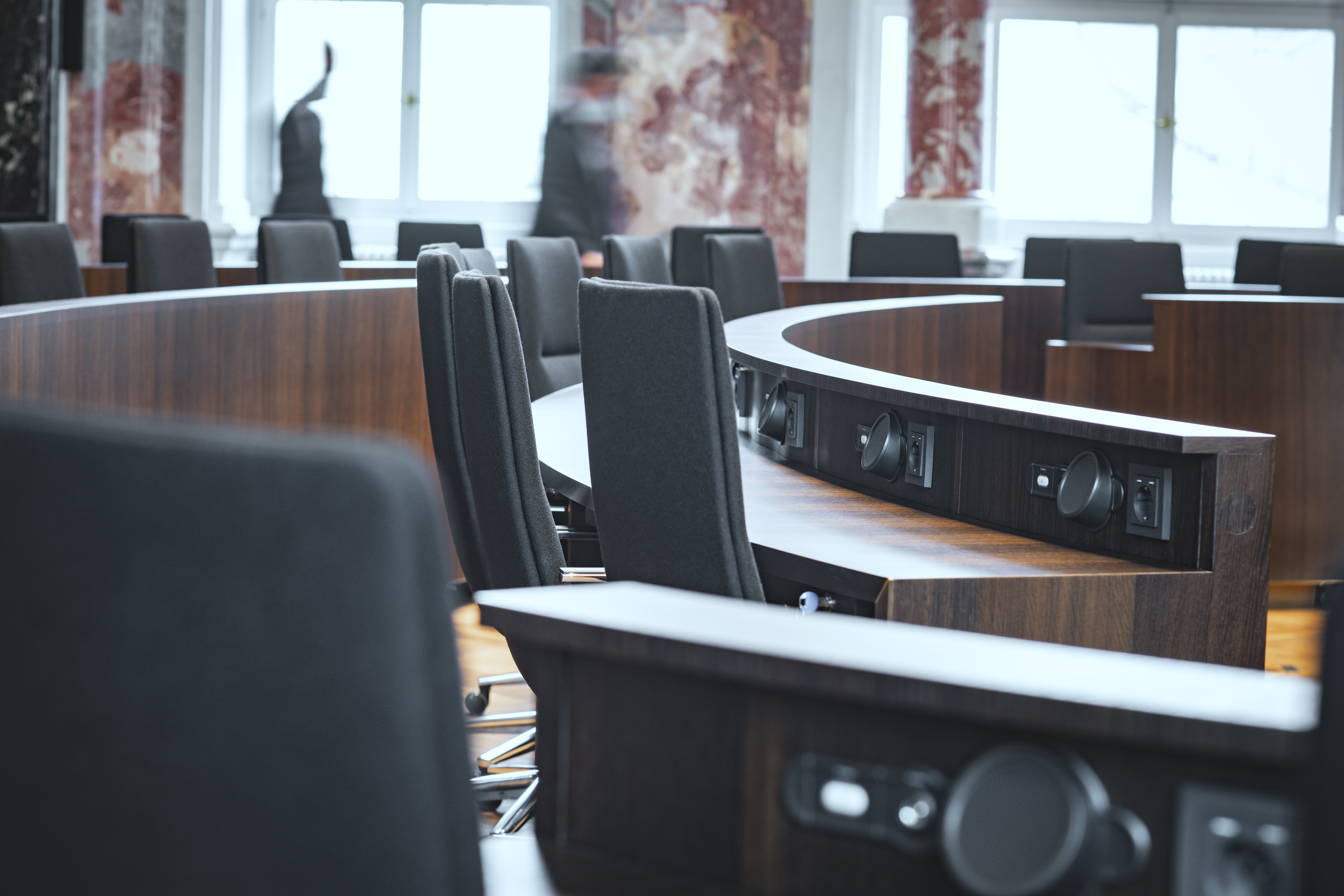 A close-up of black Sola conference chairs arranged in circular rows. They are set up around round brown wooden tables.