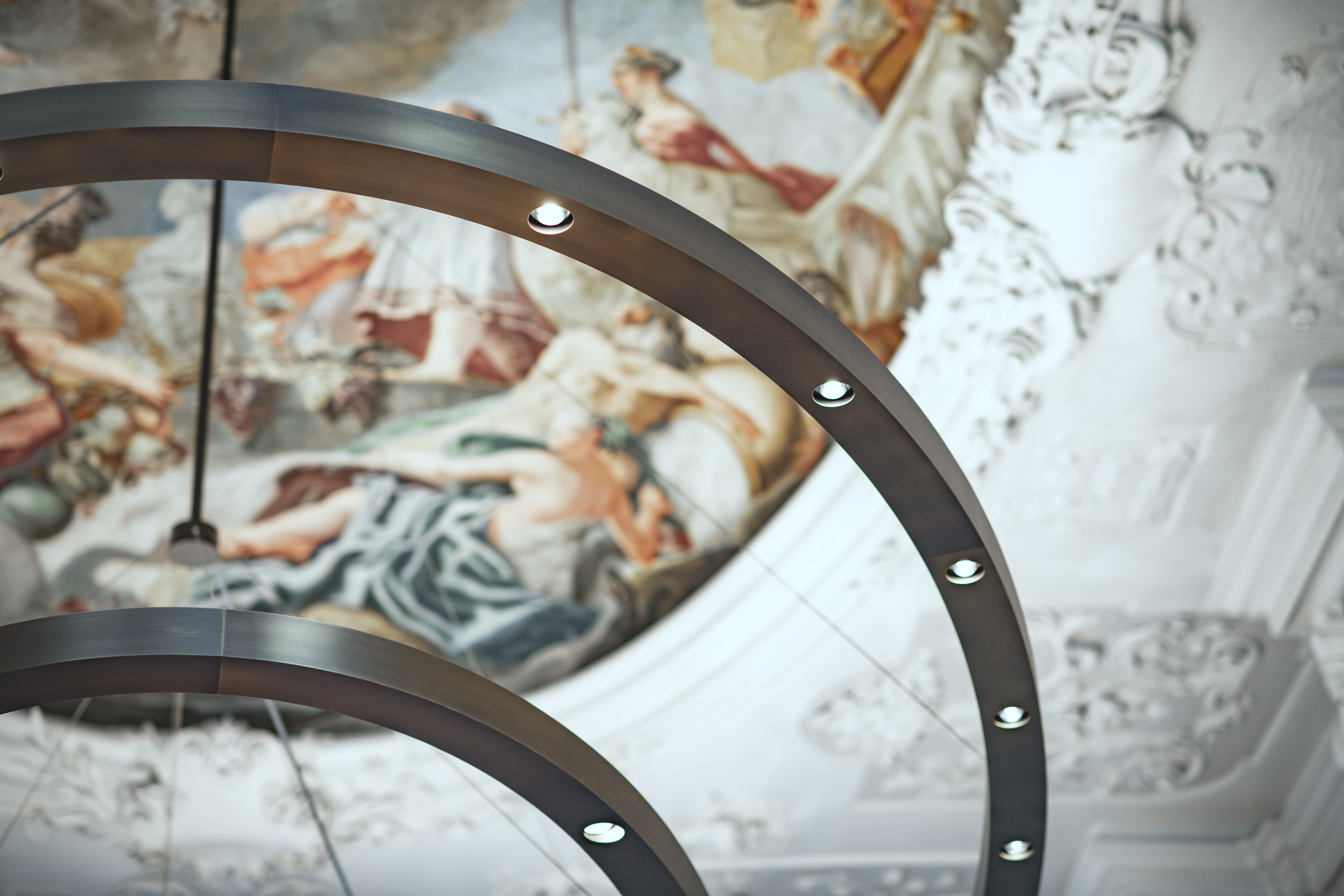 A close-up of a round ring lamp. In the background, complex wall murals can be seen.