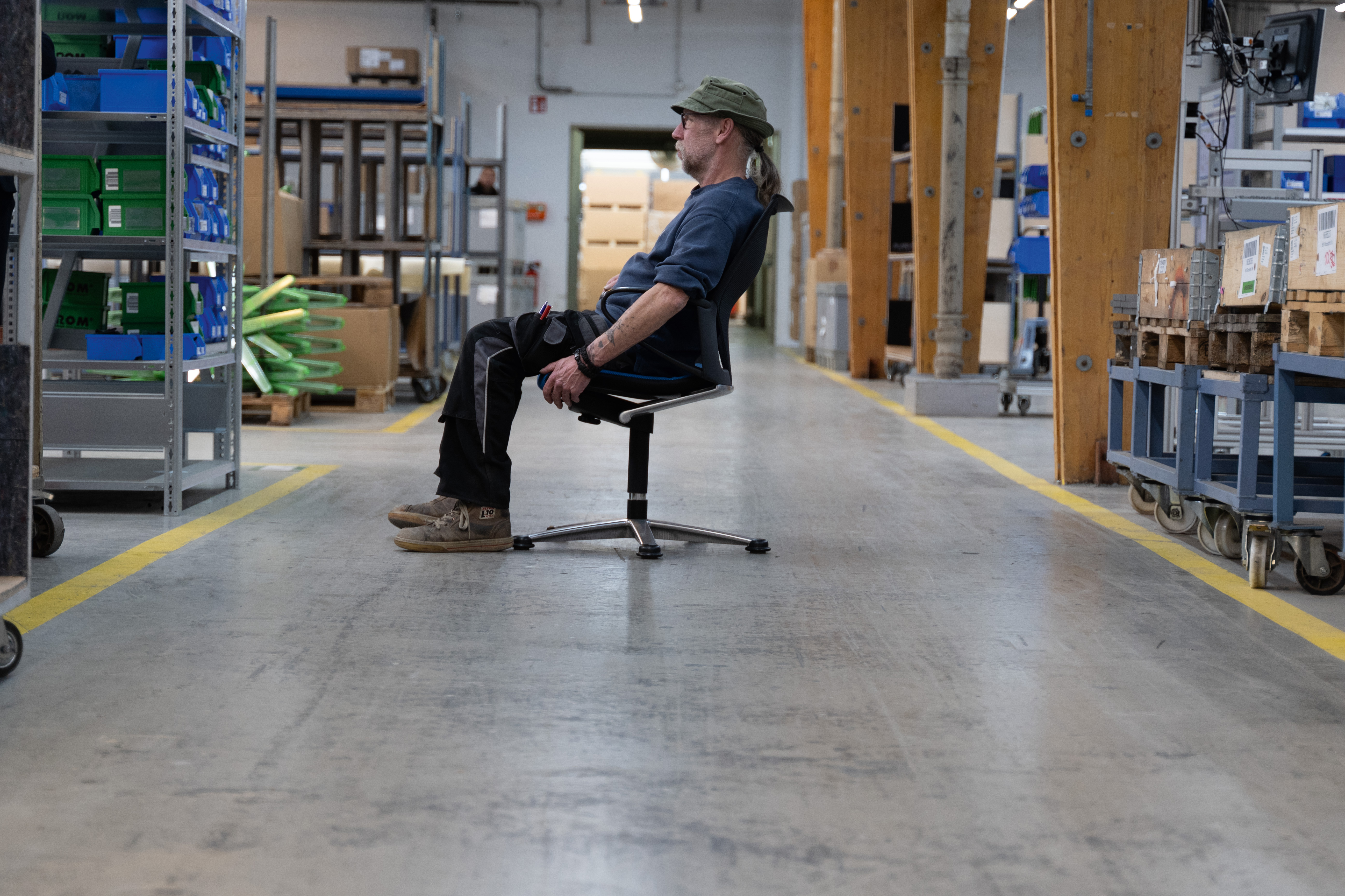 A production worker is sitting in a black Modus swivel chair located in the middle of the production hall at Wilkhahn.