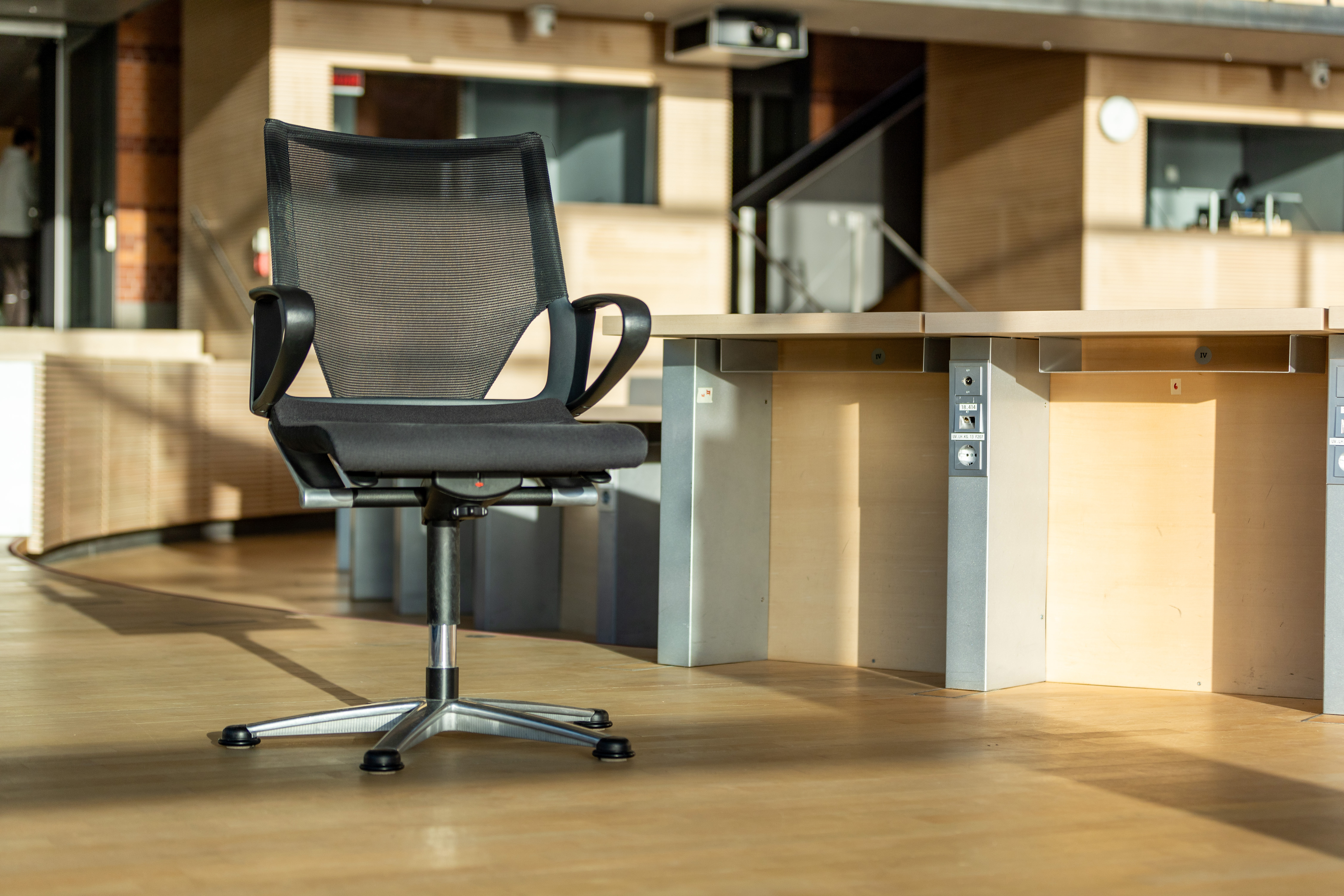 A black Modus swivel chair stands in a room where one would otherwise see only rows of wooden tables.