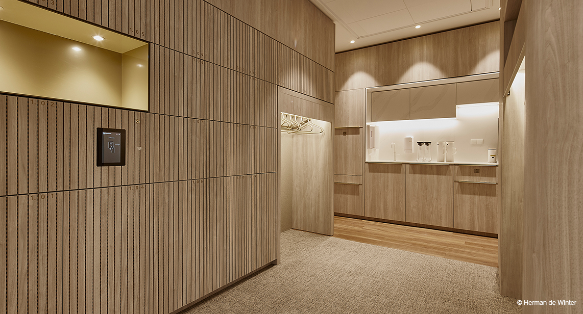 The space has the feel of an elegant coatroom or service area, featuring light wood finishes throughout and integrated lighting. The clean lines and minimalist fixtures create a calm, sophisticated atmosphere.