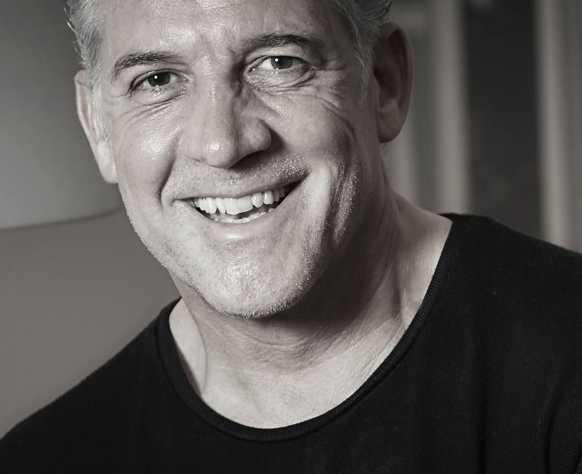 It is a black-and-white portrait of a man. He is wearing a black T-shirt and has light-colored hair.